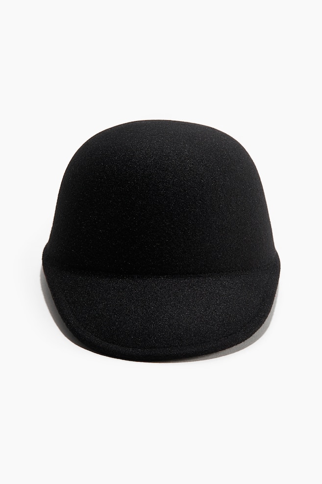 The black cap features a rounded, subtly textured crown and a short, rounded brim, facing forward. - 1