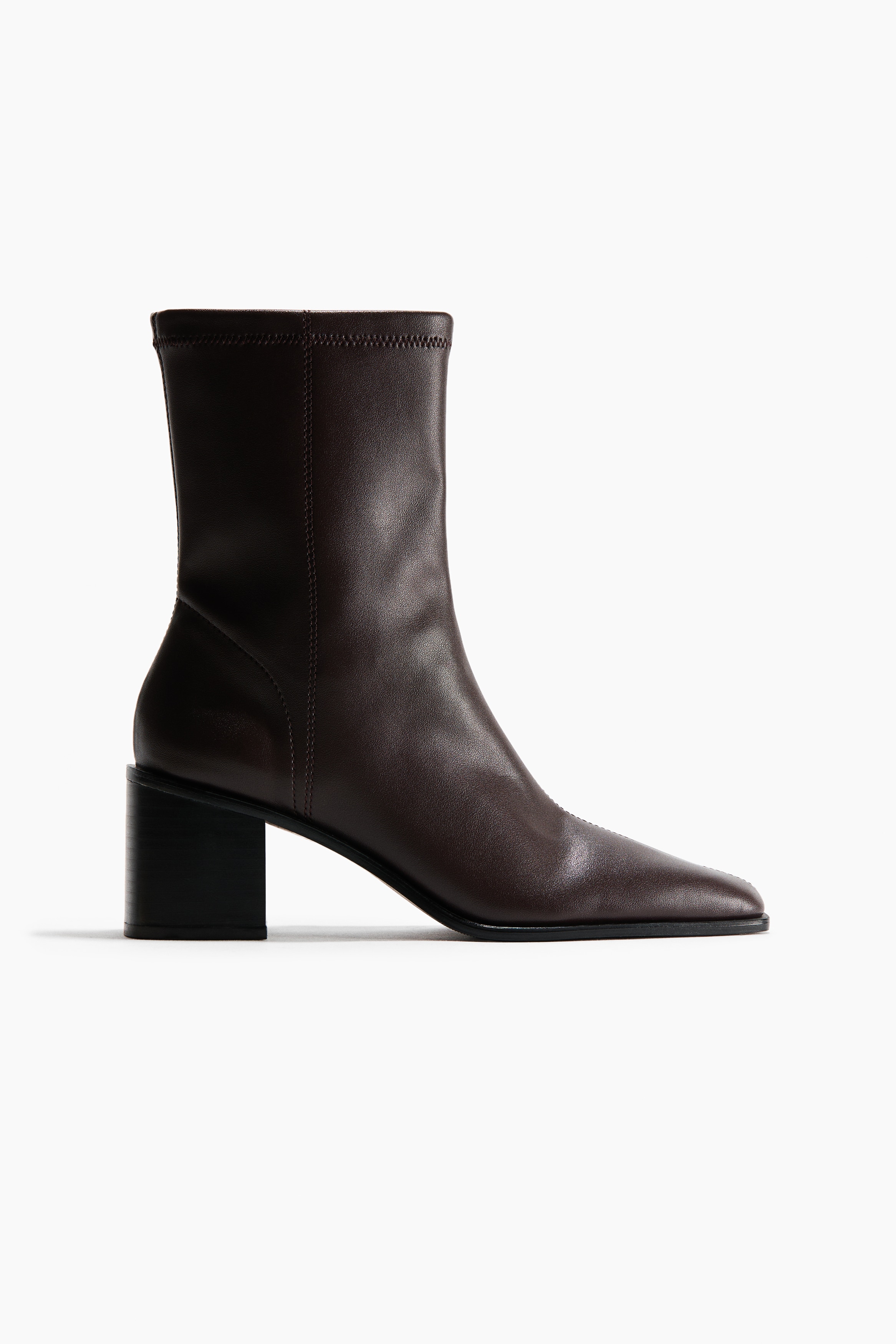 MÃ¶rkbruna ankelboots med stretchskaft, dragkedjor pÃ¥ sidan, spetsiga tÃ¥partier och blockklackar bÃ¤rs av modellen. Bootsarna Ã¤r stylade med en svepande kjol i krÃ¤mfÃ¤rgad nyans.