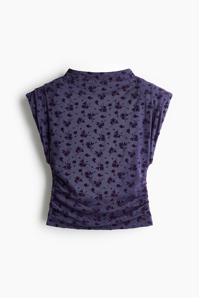 Een paarse mesh top met een all-over donker bloemmotief in flockprint wordt van voren gepresenteerd, met een hoge hals en kapmouwen met gestructureerde schouderplooien. Het kledingstuk heeft gerimpelde zijnaden die zorgen voor een gedrapeerd, geplooid effect over de taille. - 1