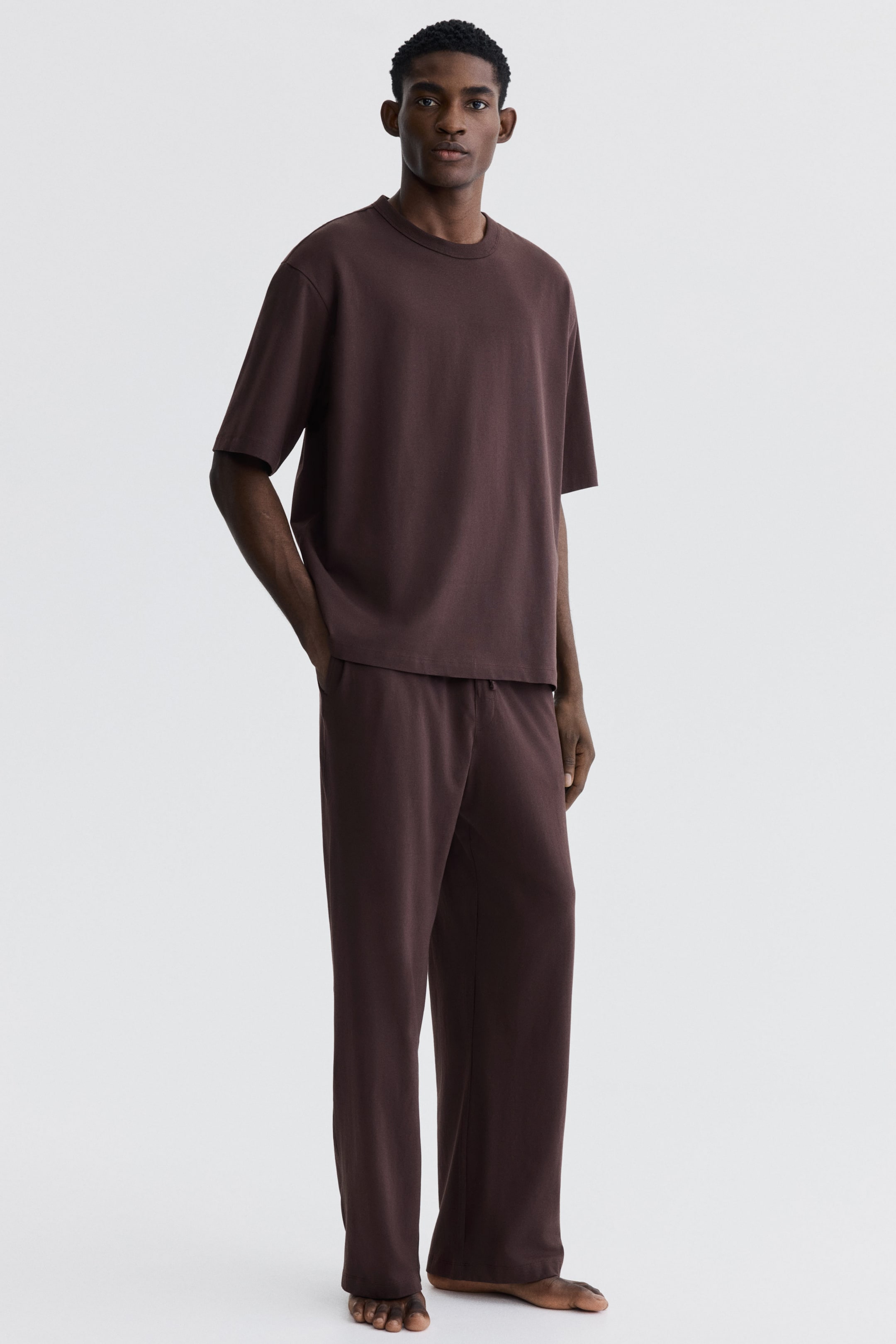 View larger image: A dark brown two-piece loungewear set is showcased, featuring a relaxed-fit, short-sleeve t-shirt with a crew neck and a straight hem, paired with matching straight-leg pants offering a relaxed, full-length silhouette.