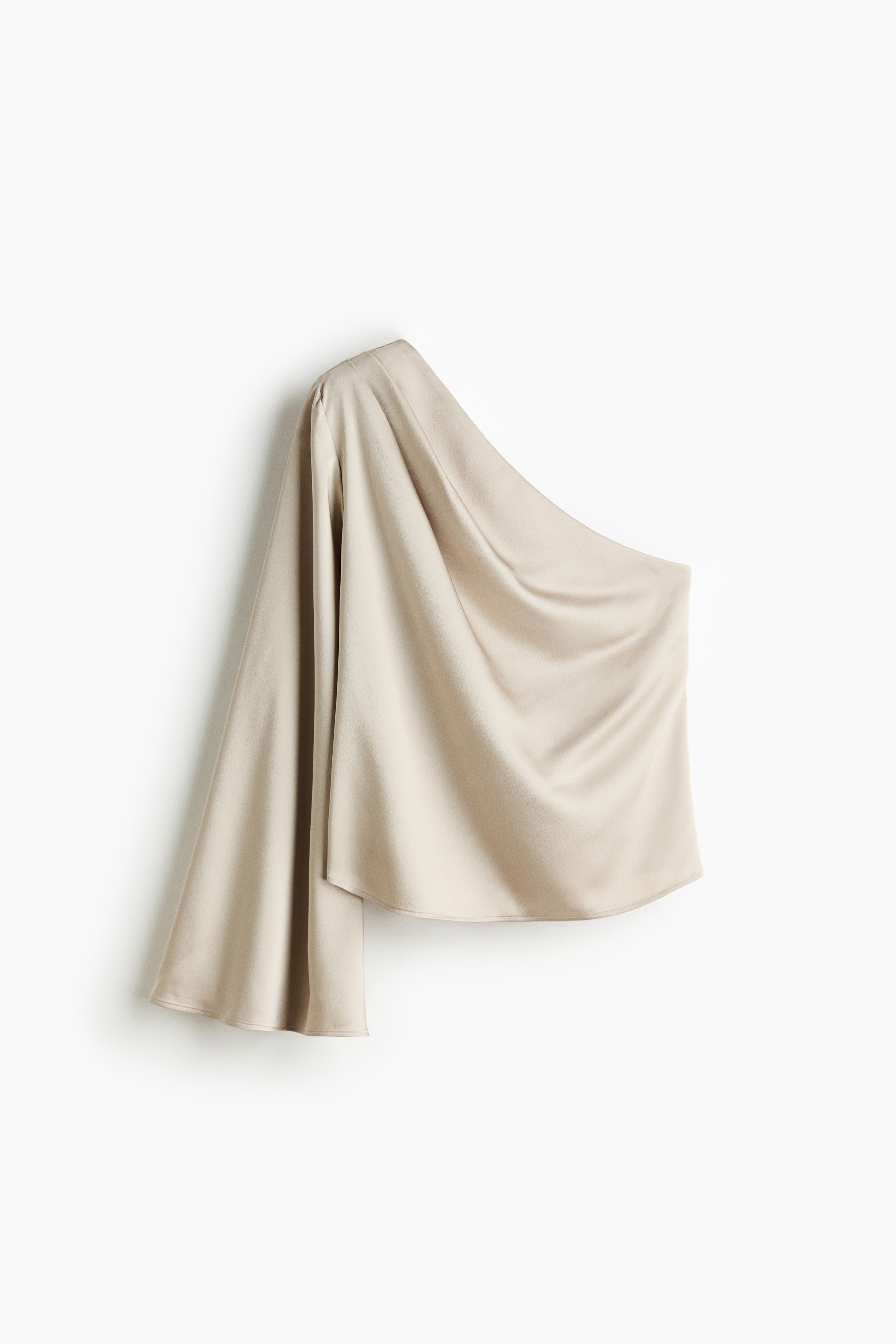 A light beige, one-shoulder top in draped satin is being worn by the model, featuring an asymmetrical neckline and a single long, wide sleeve. The top is styled with black trousers, showcasing the draped fabric across the back.