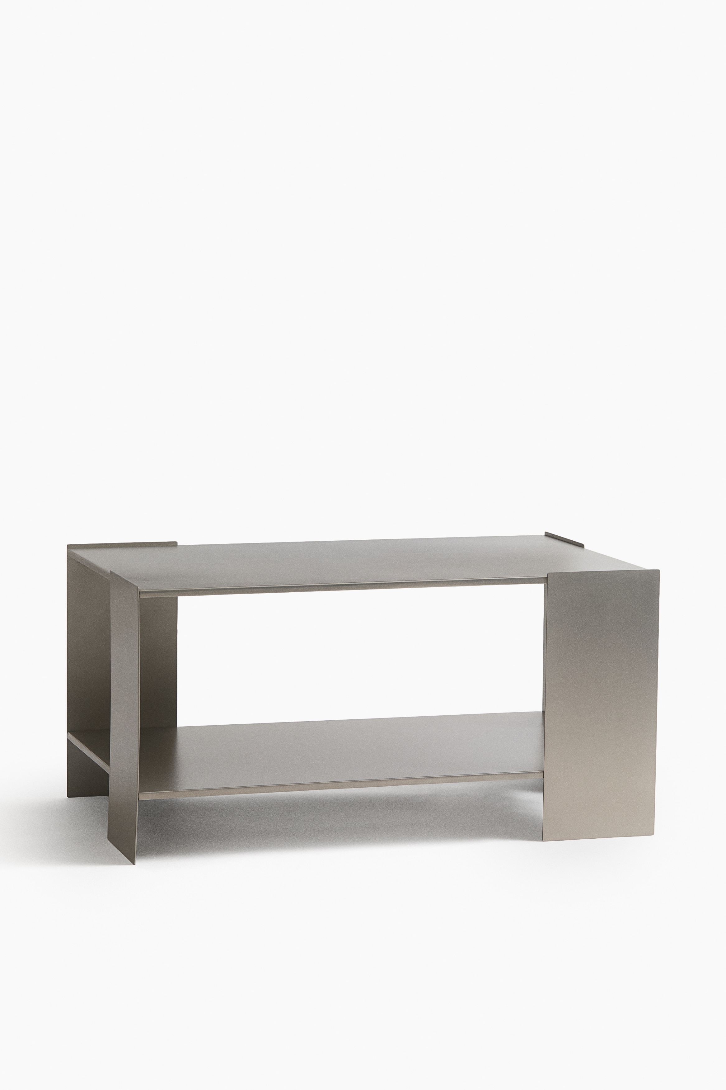 A dark grey metal coffee table is showcasing a geometric design from the front, featuring a flat rectangular top, an integrated lower shelf, and asymmetrical vertical support panels. A light-coloured, rounded ceramic vase is resting on its top surface.