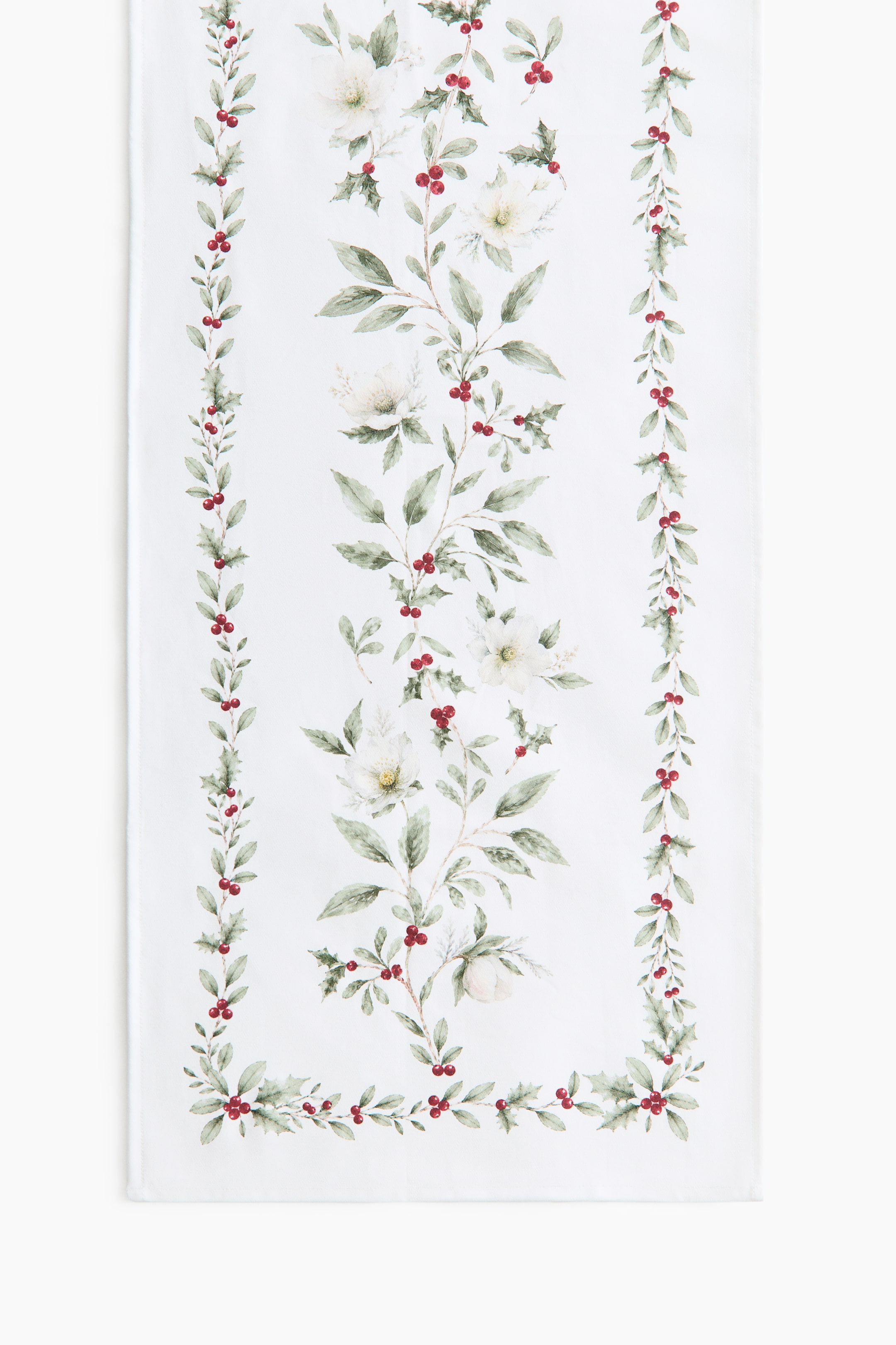 Visualizza immagine più grande: Un runner da tavola in twill di cotone bianco è mostrato in una vista frontale piatta, con una stampa botanica di foglie verdi, bacche rosse e fiori bianchi. Il design è composto da una vite rampicante centrale affiancata da due stretti bordi verticali e da un bordo orizzontale coordinato lungo l’orlo inferiore.