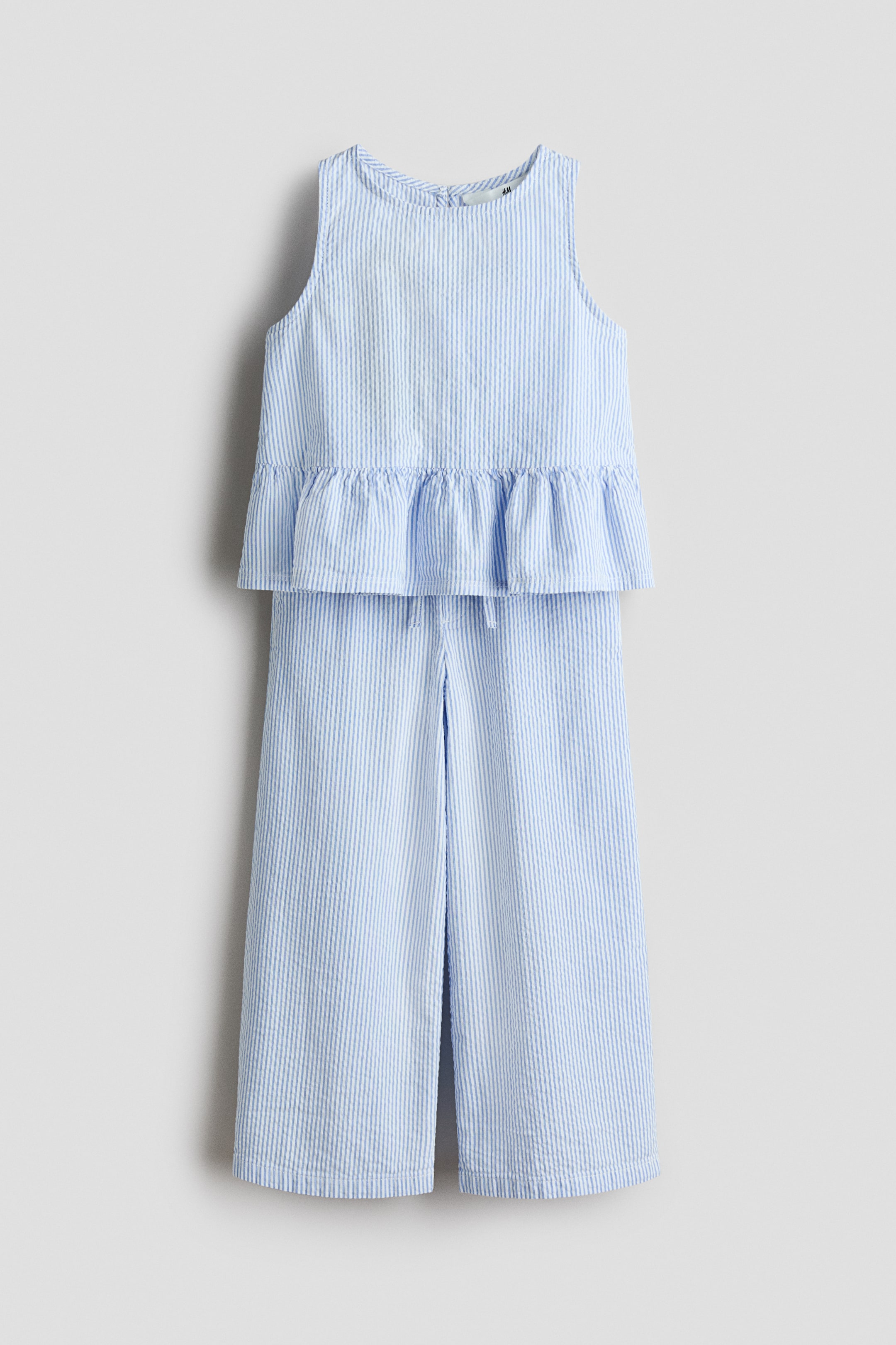 View larger image: The outfit is a light blue and white striped seersucker two-piece set, presented facing FRONT. The sleeveless top is featuring a round neckline and a ruffled peplum hem. The matching wide-leg pants are designed with a cropped length and a drawstring waist.