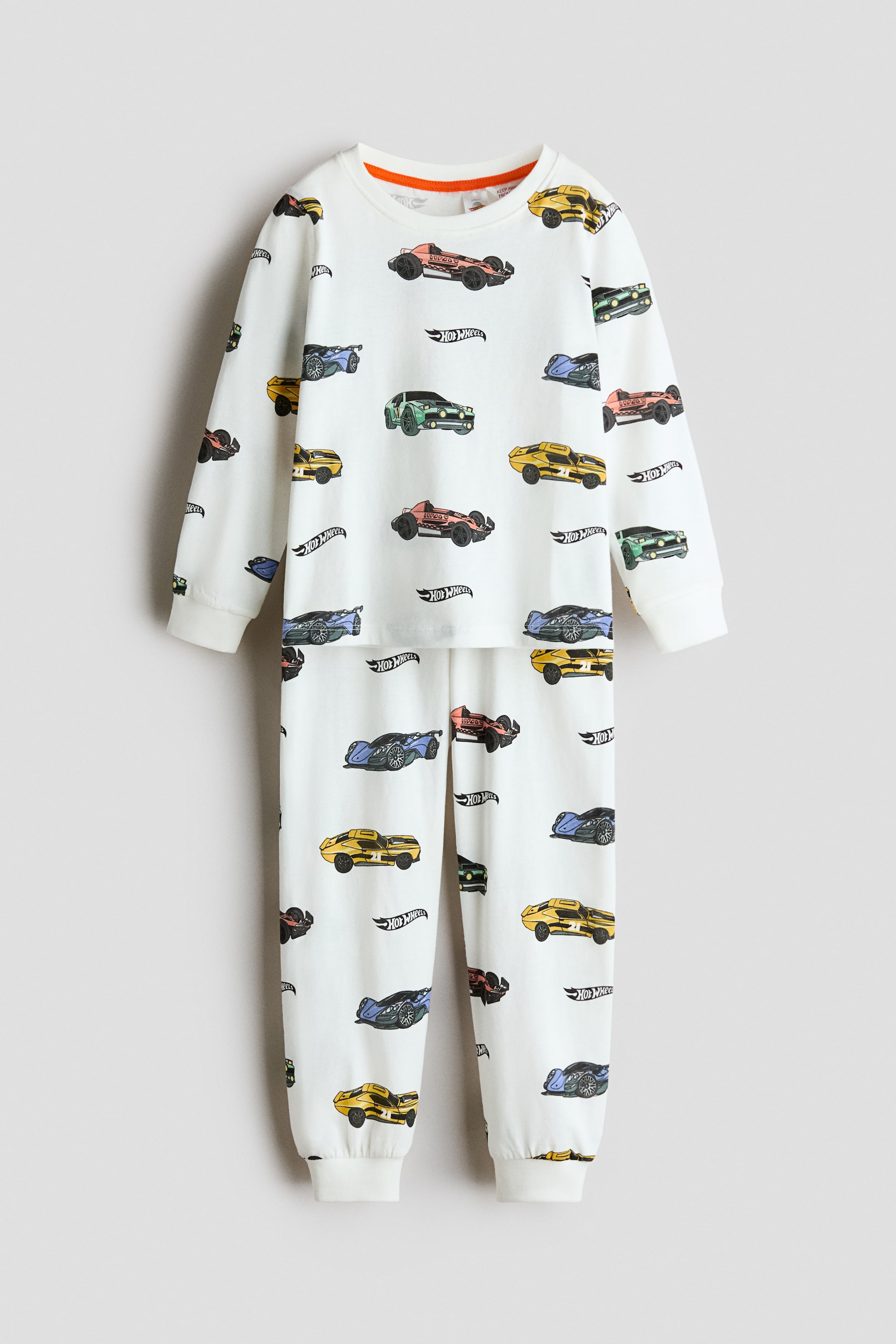 View larger image: Pyjamas featuring a long-sleeved top and matching bottoms are displaying an all-over print of colourful cars and Hot Wheels logos on a white background. The top is showing a round, ribbed neckline and ribbed cuffs, while the bottoms are featuring ribbed hems.