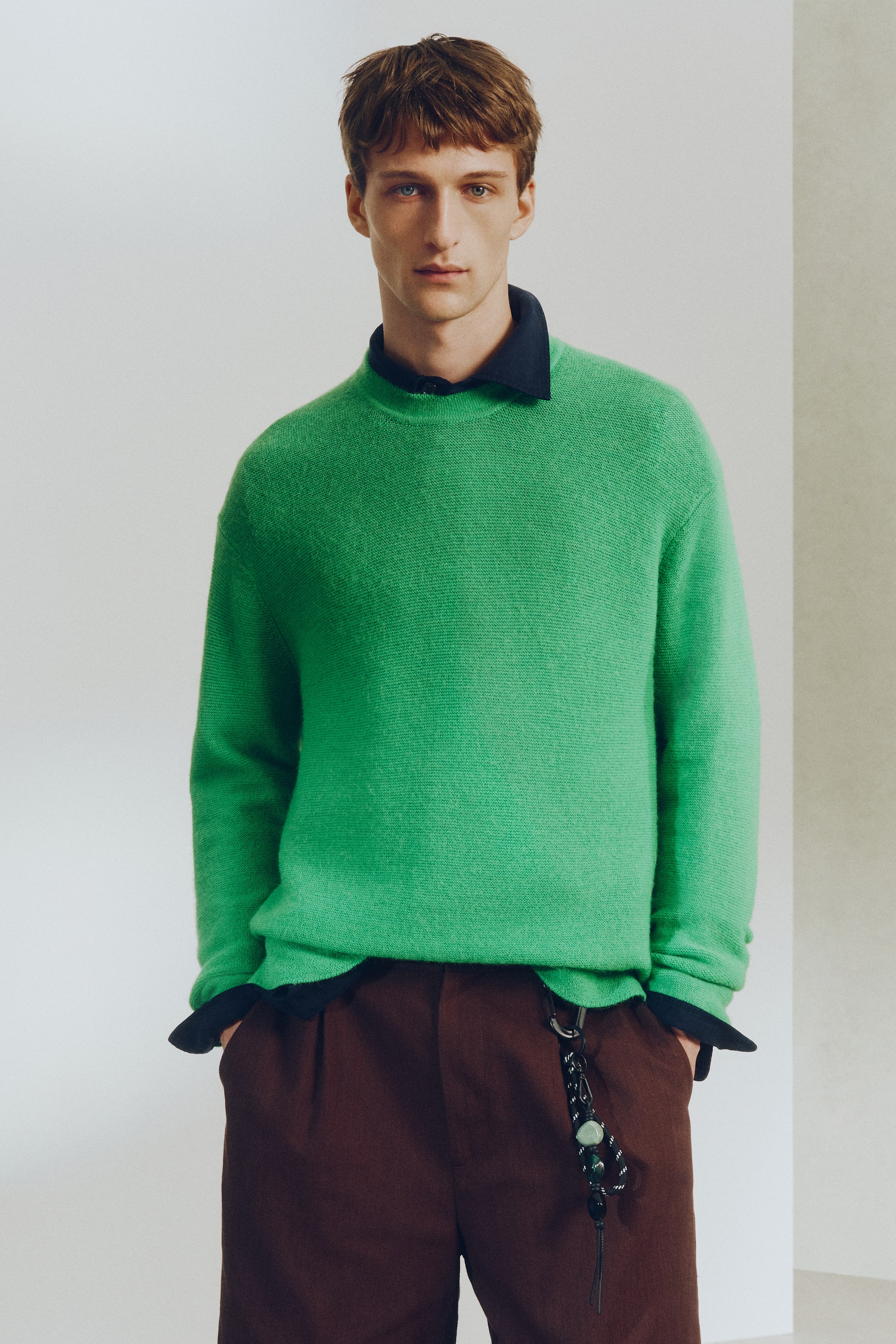 View larger image: A vibrant green crewneck jumper is facing forward, showcasing a visible knit texture and a relaxed fit. A dark blue shirt collar is visible at the neck, with its cuffs showing at the wrists and hem, layered beneath the jumper.