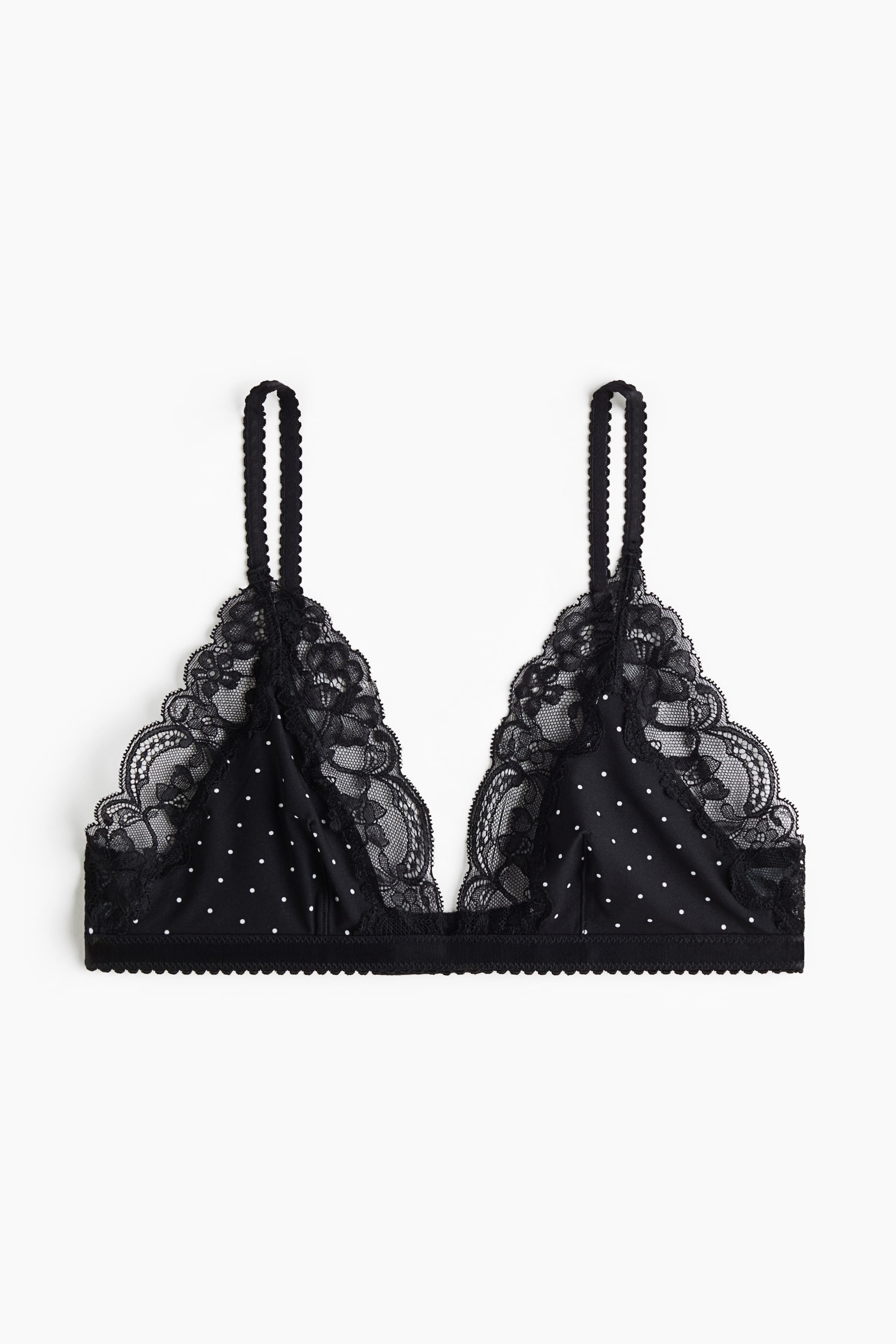 Grotere afbeelding bekijken: Een zwarte triangelbralette is van voren gefotografeerd, met witte stippen op de stoffen cups en verfijnde zwarte kanten bies langs de diepe halslijn. Het ontwerp is voorzien van getextureerde, geschulpte schouderbandjes en een bijpassende geschulpte elastische onderbusteband.