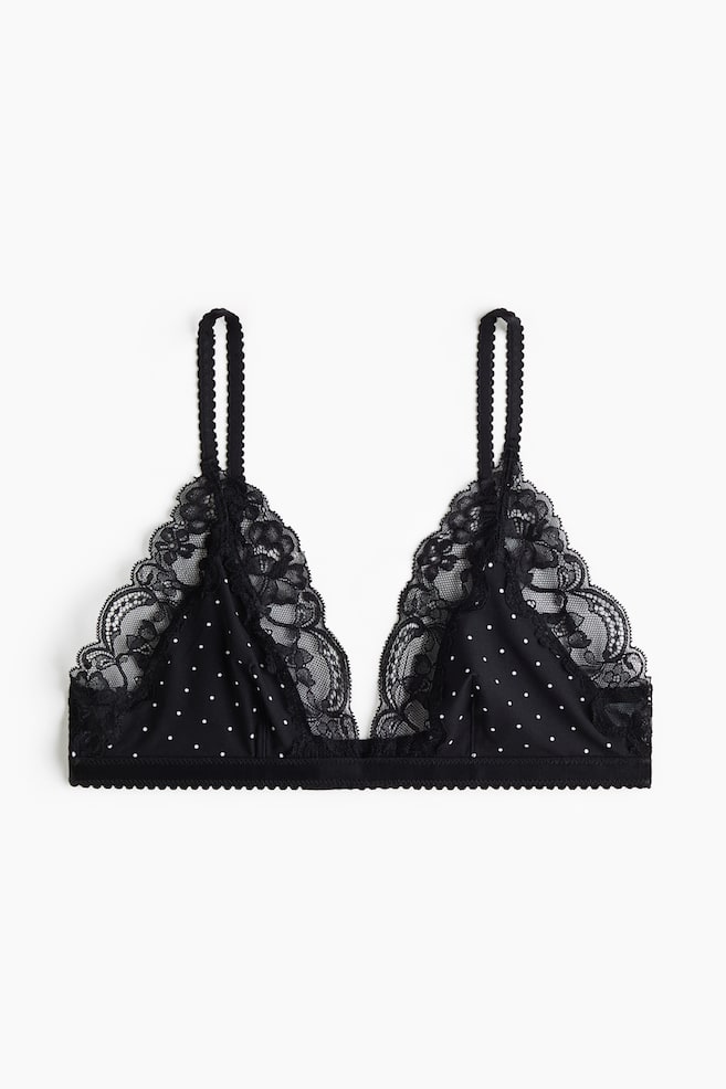 Ein schwarzer Triangel-Bralette ist frontal ausgerichtet und zeigt weiÃe Polka Dots auf den Stoffcups sowie eine filigrane schwarze Spitzenborte entlang des tiefen Ausschnitts. Das Design verfÃ¼gt Ã¼ber strukturierte, gewellte TrÃ¤ger und ein passendes gewelltes elastisches Unterbrustband. - 1