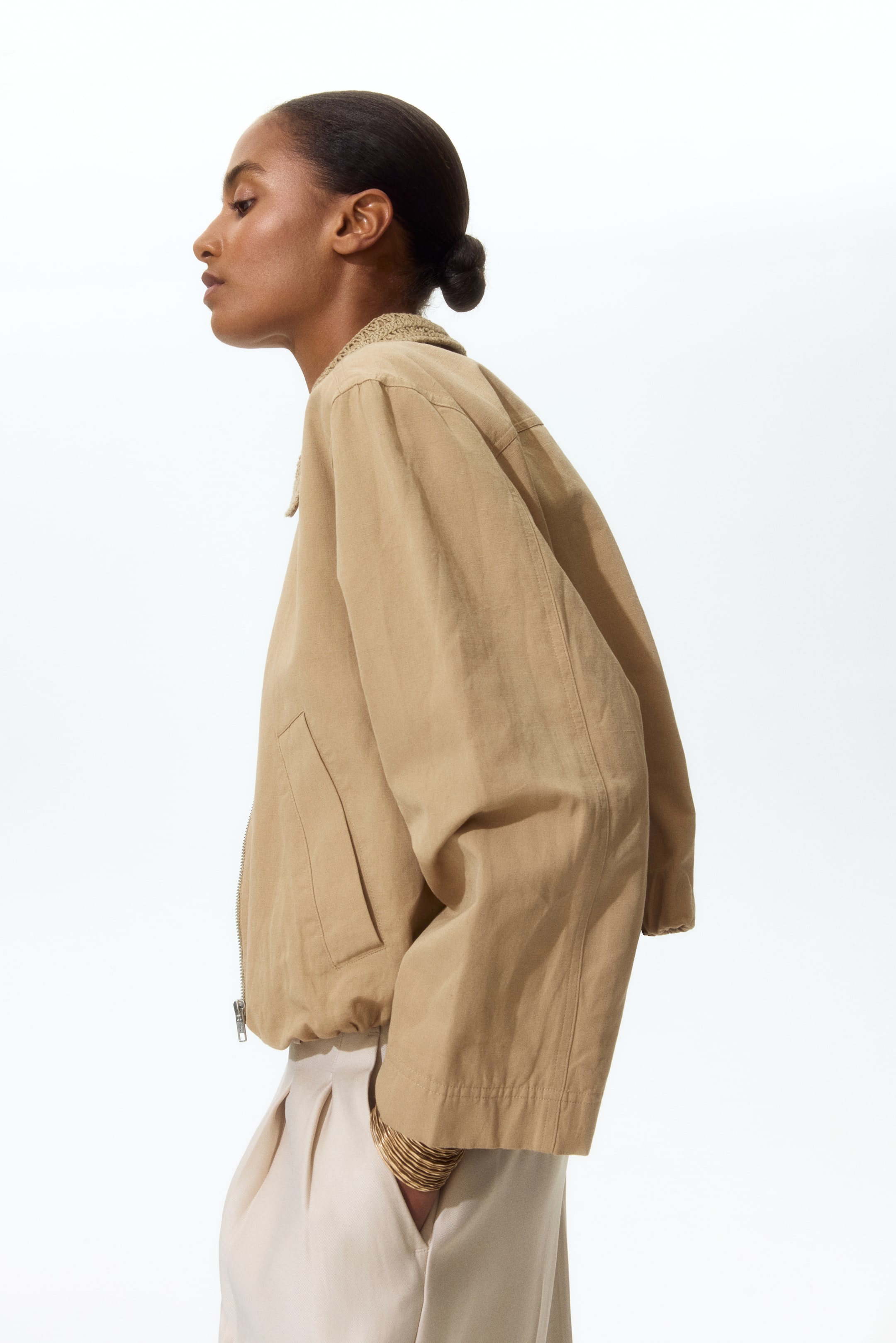 View larger image: A light brown jacket is facing left, showcasing a textured stand-up collar and a front zipper closure. It features long sleeves and flat welt pockets, with a gathered hemline resting at the waist.
