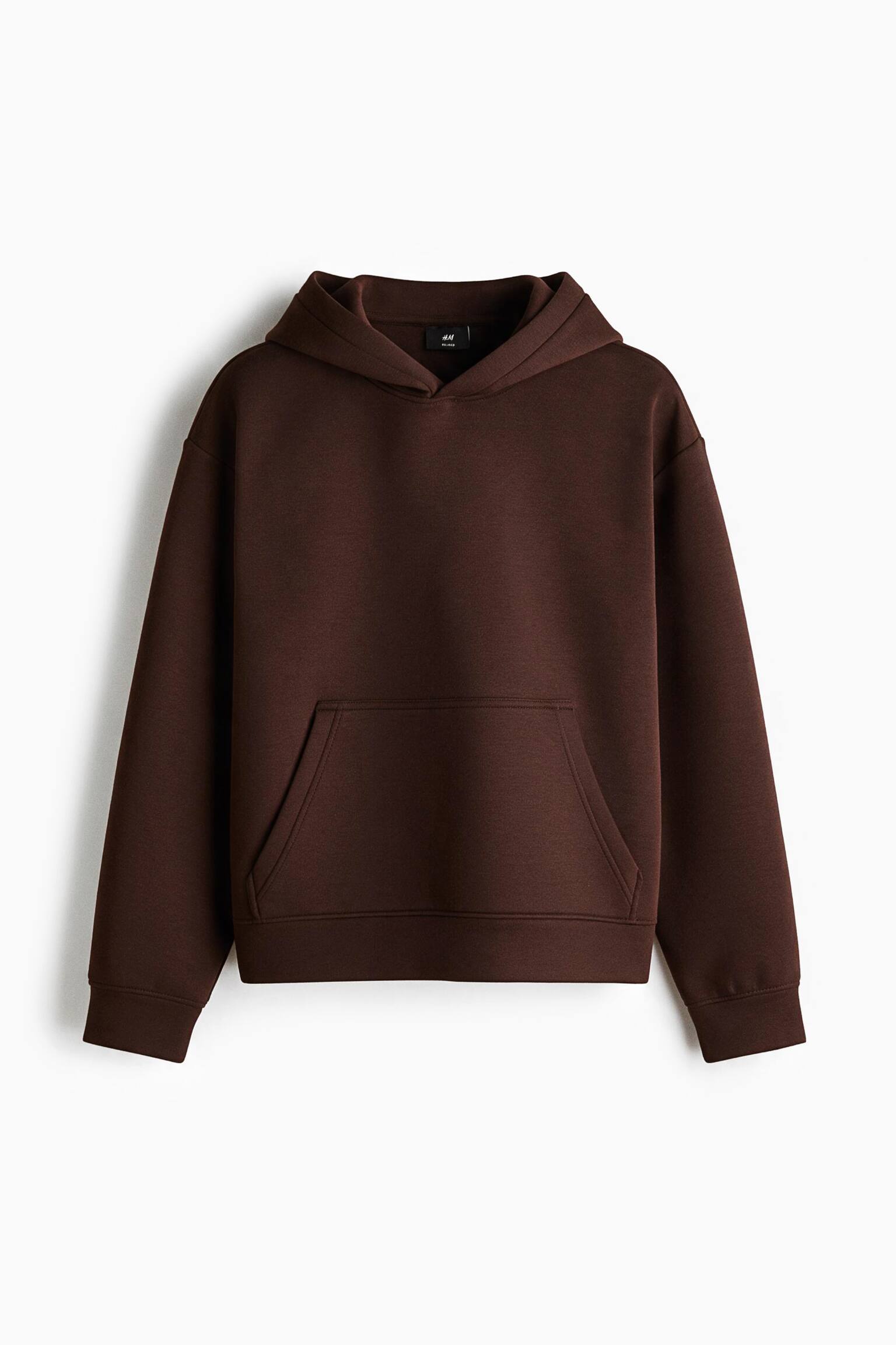 A dark brown hoodie in a smooth scuba fabric is shown from the front, featuring a relaxed fit with a double-layered hood and dropped shoulders. The hoodie has a front kangaroo pocket and wide ribbed cuffs and hem.