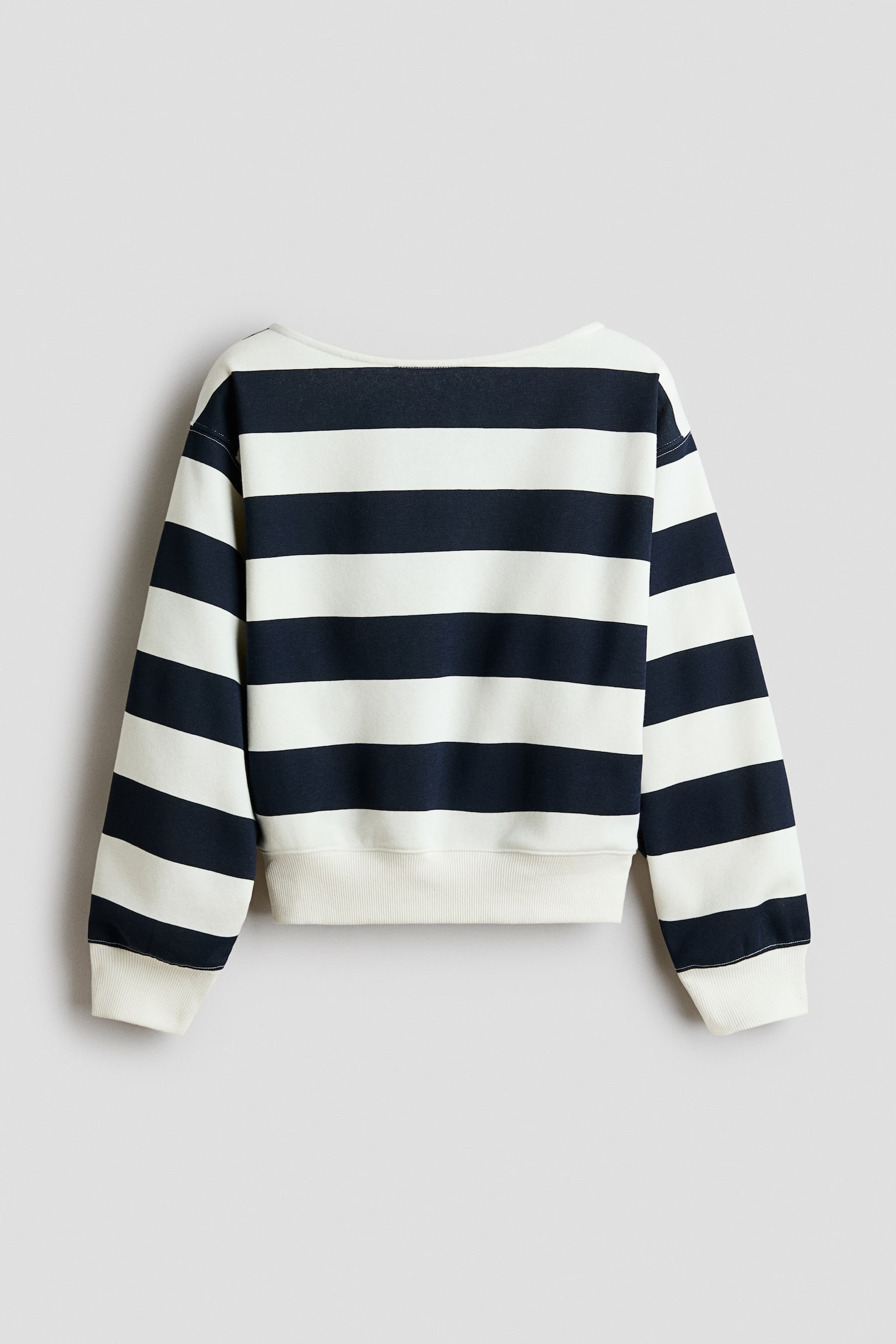 En lÃ¥ngÃ¤rmad sweatshirt med djÃ¤rva horisontella rÃ¤nder i marinblÃ¥tt och benvitt visas bakifrÃ¥n. Den har en bred halsringning, nedhasade axlar samt enfÃ¤rgade ribbade muddar och nederkant i benvitt.