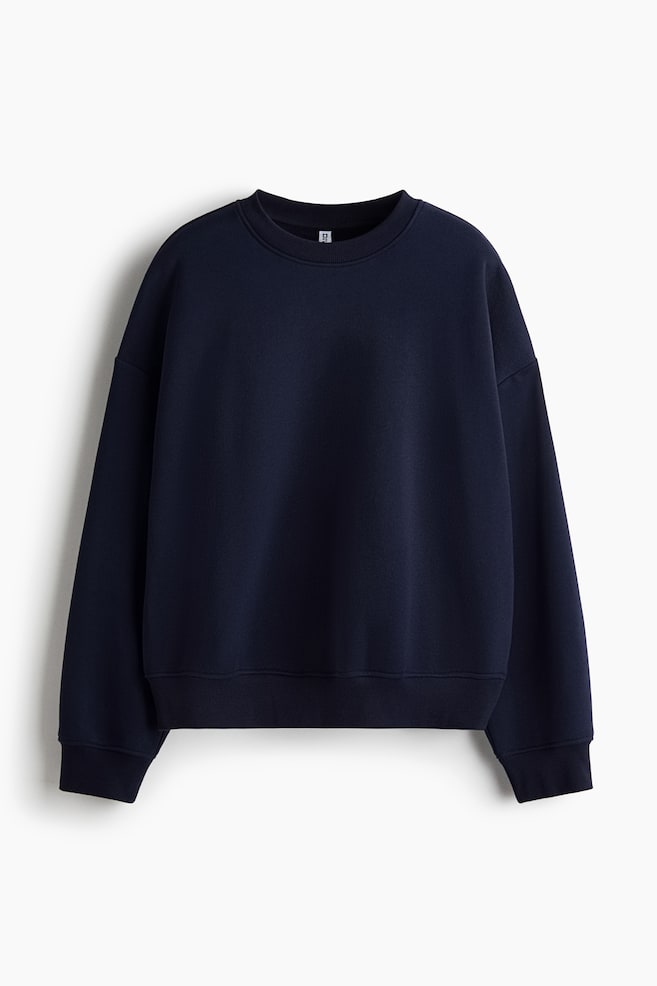 A dark navy blue oversized sweatshirt is shown from the front, featuring a rib-trimmed crew neckline, dropped shoulders, and long sleeves. The sweatshirt is finished with ribbed cuffs and a ribbed hem. - 1