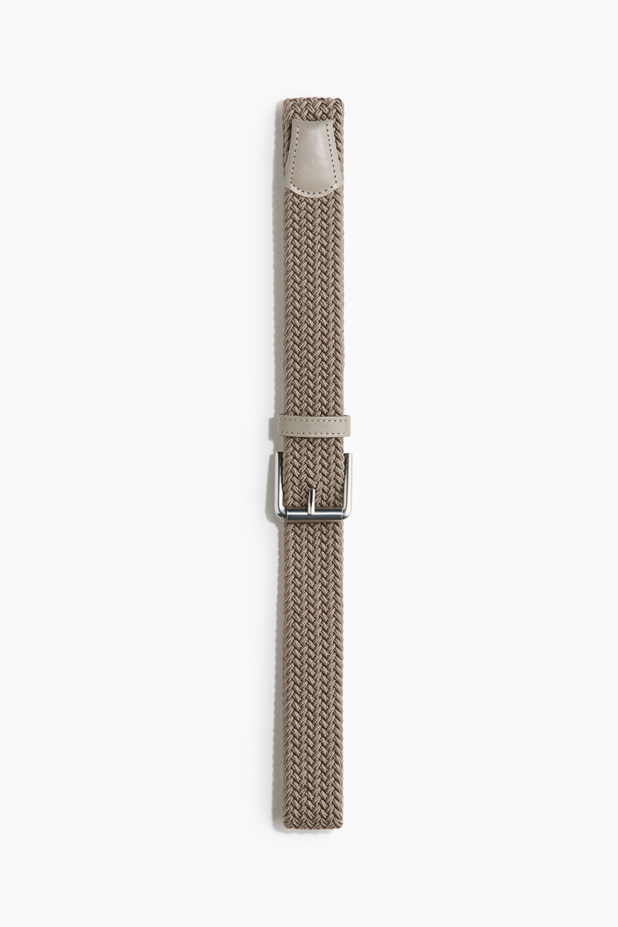 Visa större bild: Ett ljusbrunt flätat elastiskt tygbälte presenteras platt, med ljusbeige belagda detaljer vid ändarna och runt ett silverfärgat metallspänne.