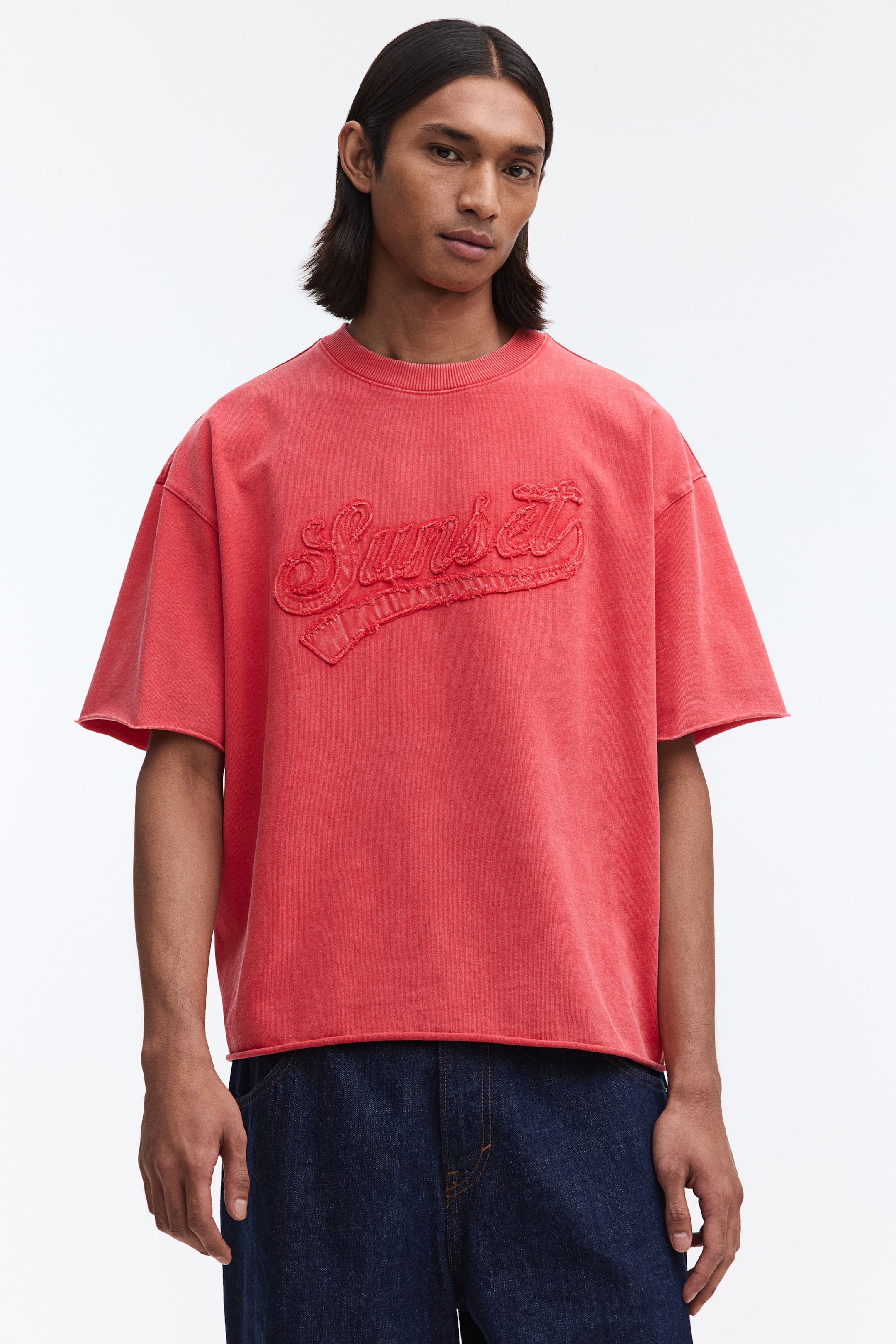Ampliar la imagen: Una sudadera roja de manga corta presenta un diseño bordado de la palabra "Sunset" en el frente, con un parche de borde sin rematar debajo. Está diseñada con un cuello redondo acanalado, hombros caídos y puños y dobladillo de borde sin rematar, ofreciendo un ajuste holgado.