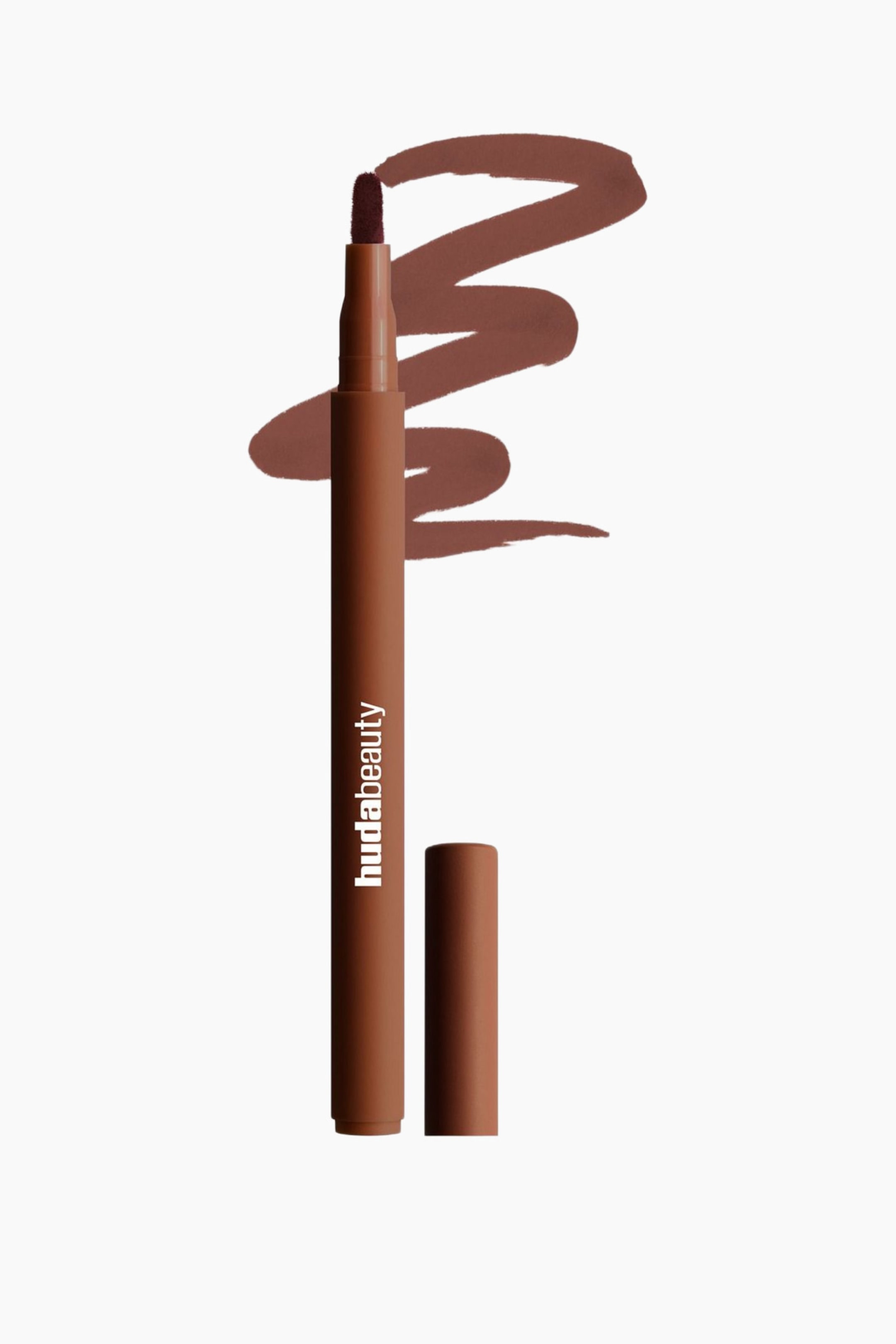 Visa större bild: En brun Huda Beauty-läppmarkör står upprätt och lätt vinklad åt höger, med sin mörkbruna filtspets synlig. Det matchande locket vilar horisontellt intill basen, och ett vågformat prov av den mörkbruna produkten är draget bakom den.