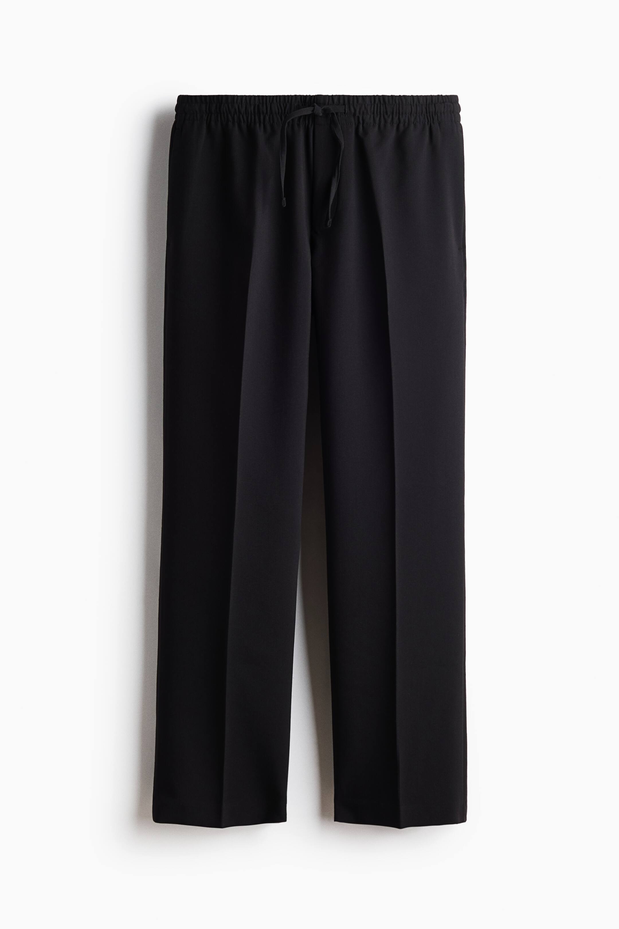 Größeres Bild anzeigen: Schwarze Hose in Frontansicht mit elastischem Bund und mittigem Kordelzug. Die Hose zeigt einen geraden Beinverlauf mit markanten vertikalen Bügelfalten auf der Vorderseite jedes Hosenbeins sowie dezenten Seitentaschen.