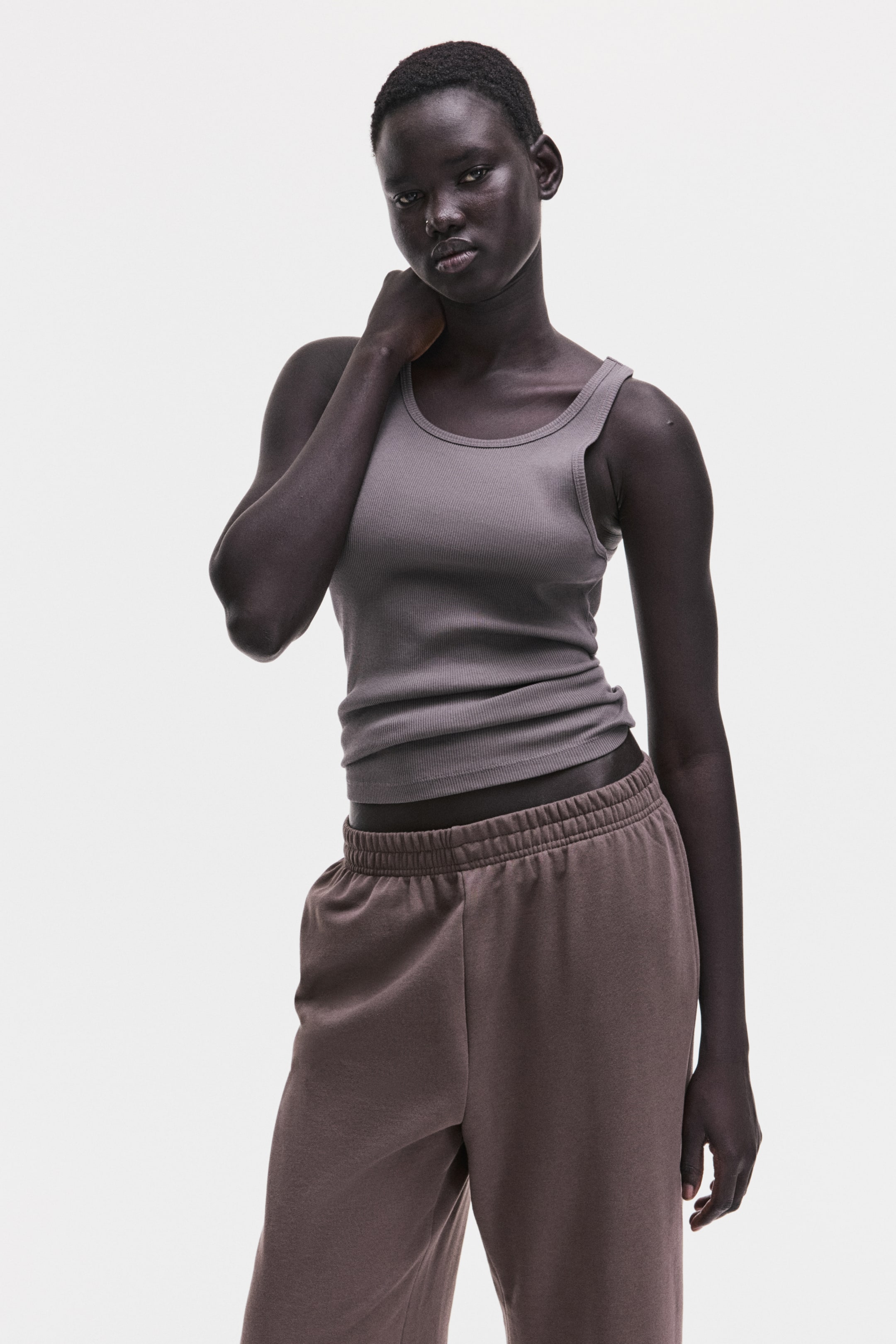 View larger image: A slate grey ribbed tank top fits closely to the body, featuring a scoop neck and wide straps. Dark brown sweatpants feature an elastic waistband and a relaxed fit.