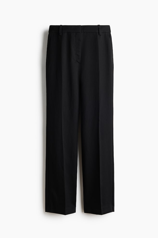 A pair of black twill trousers is shown from the front, featuring a high waist with belt loops and a concealed zip fly. The design showcases straight legs with sharp vertical creases down the centre and diagonal side pockets. - 1