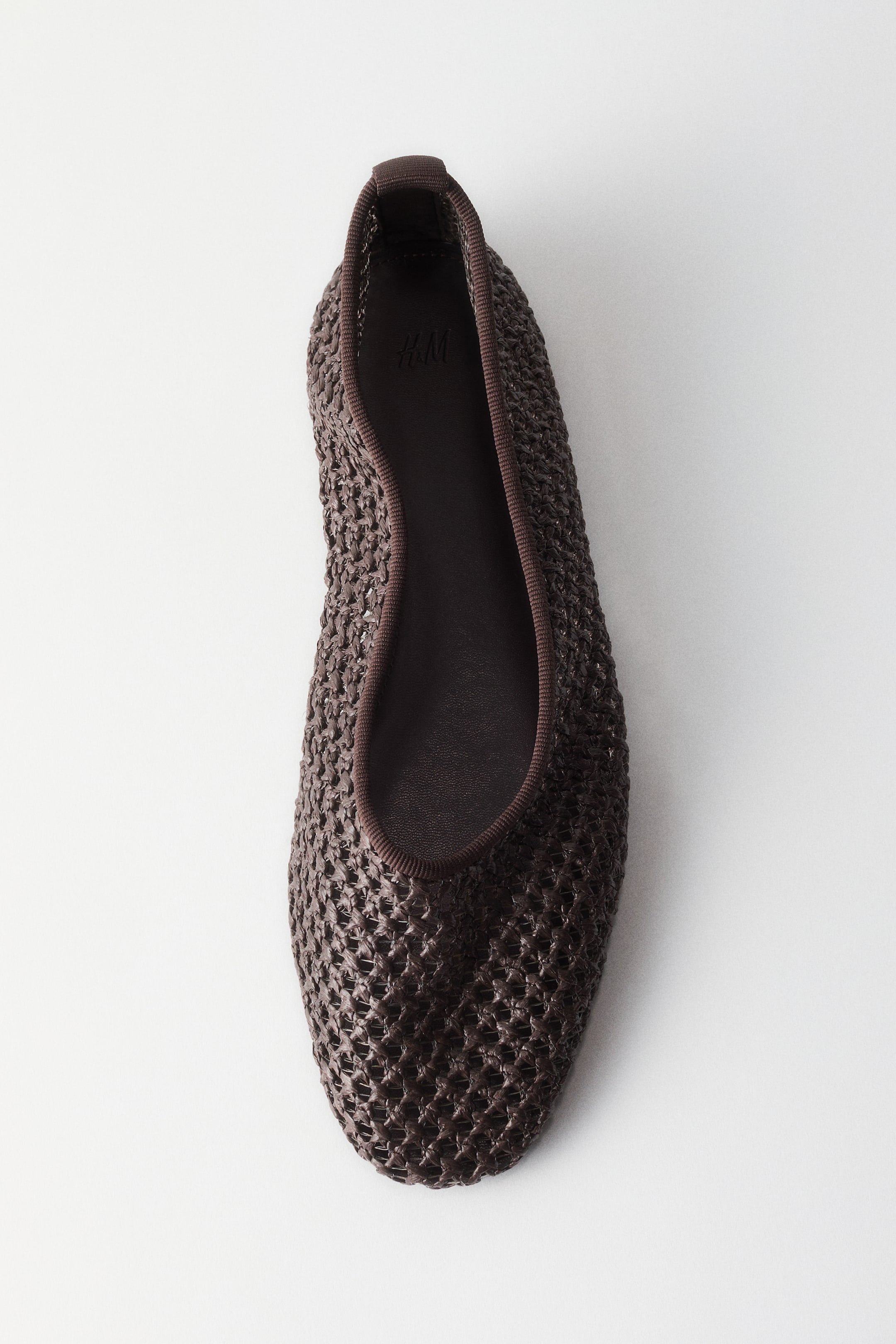 Agrandir l'image: Une ballerine marron foncé est posée à plat, vue directement d'en haut, avec son bout pointant vers la droite. Elle met en valeur une tige tissée, une semelle intérieure lisse marron foncé, et une bordure élastique marron foncé le long de l'ouverture.