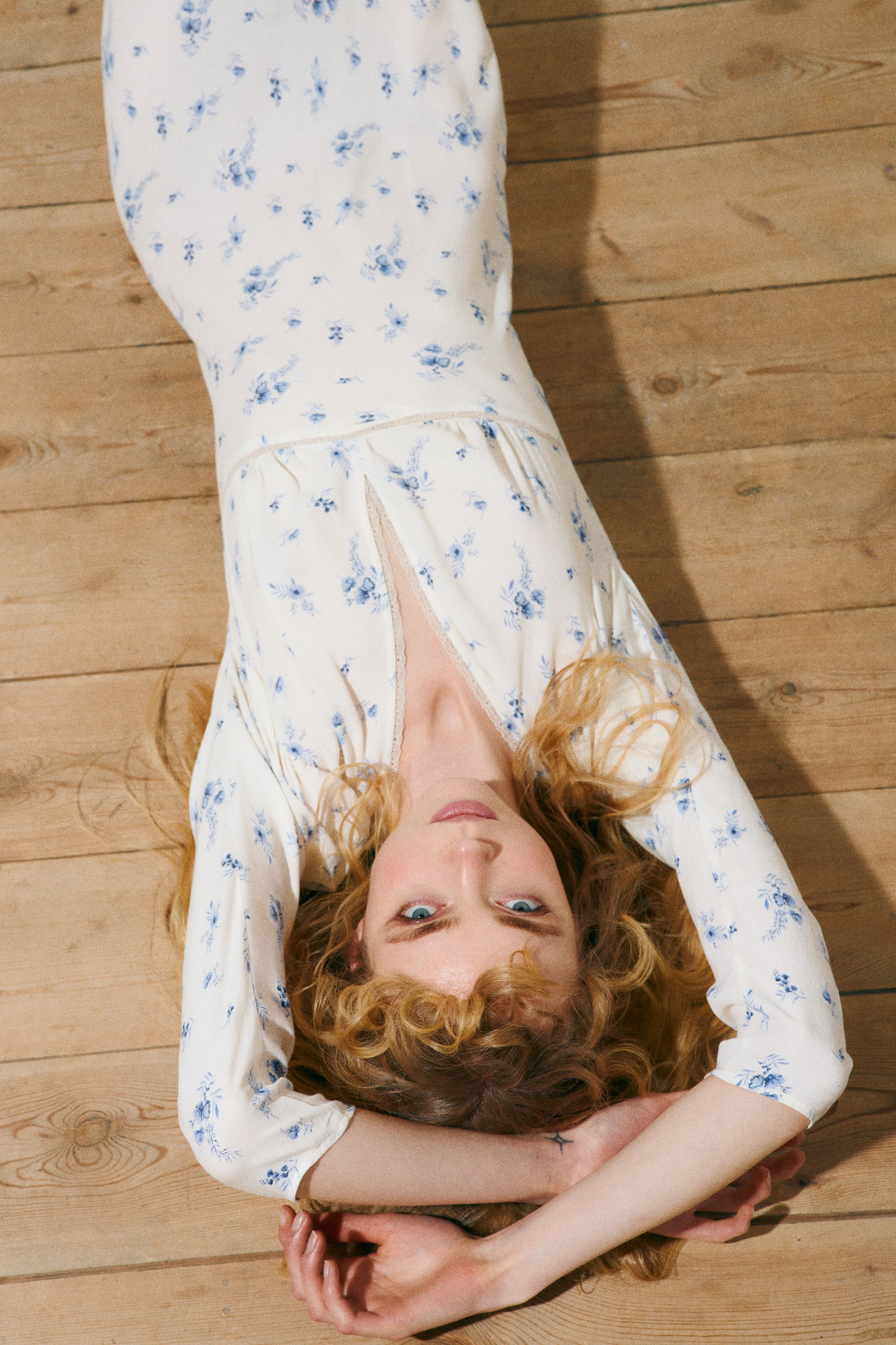 Ampliar la imagen: Se muestra un vestido blanco con estampado de flores azules; presenta un escote en V con ribete de encaje y una cintura imperio fruncida con ribete de encaje. Se aprecian mangas largas y una falda fluida.