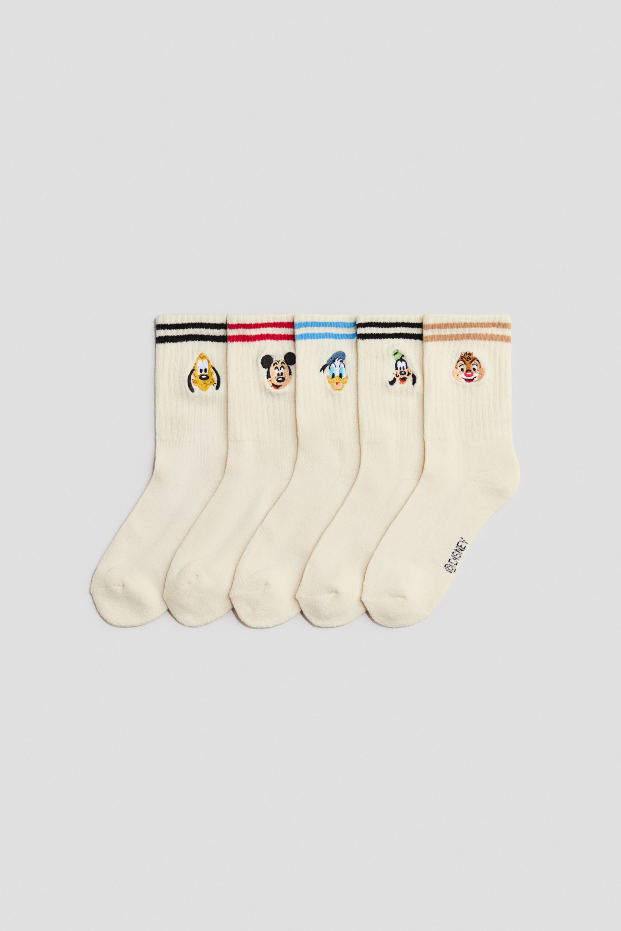View larger image: Five cream-coloured crew socks are lying flat in a row, presenting their FRONT. Each sock is featuring two horizontal stripes near the ribbed cuff in varying colours and an embroidered Disney character face below the stripes.