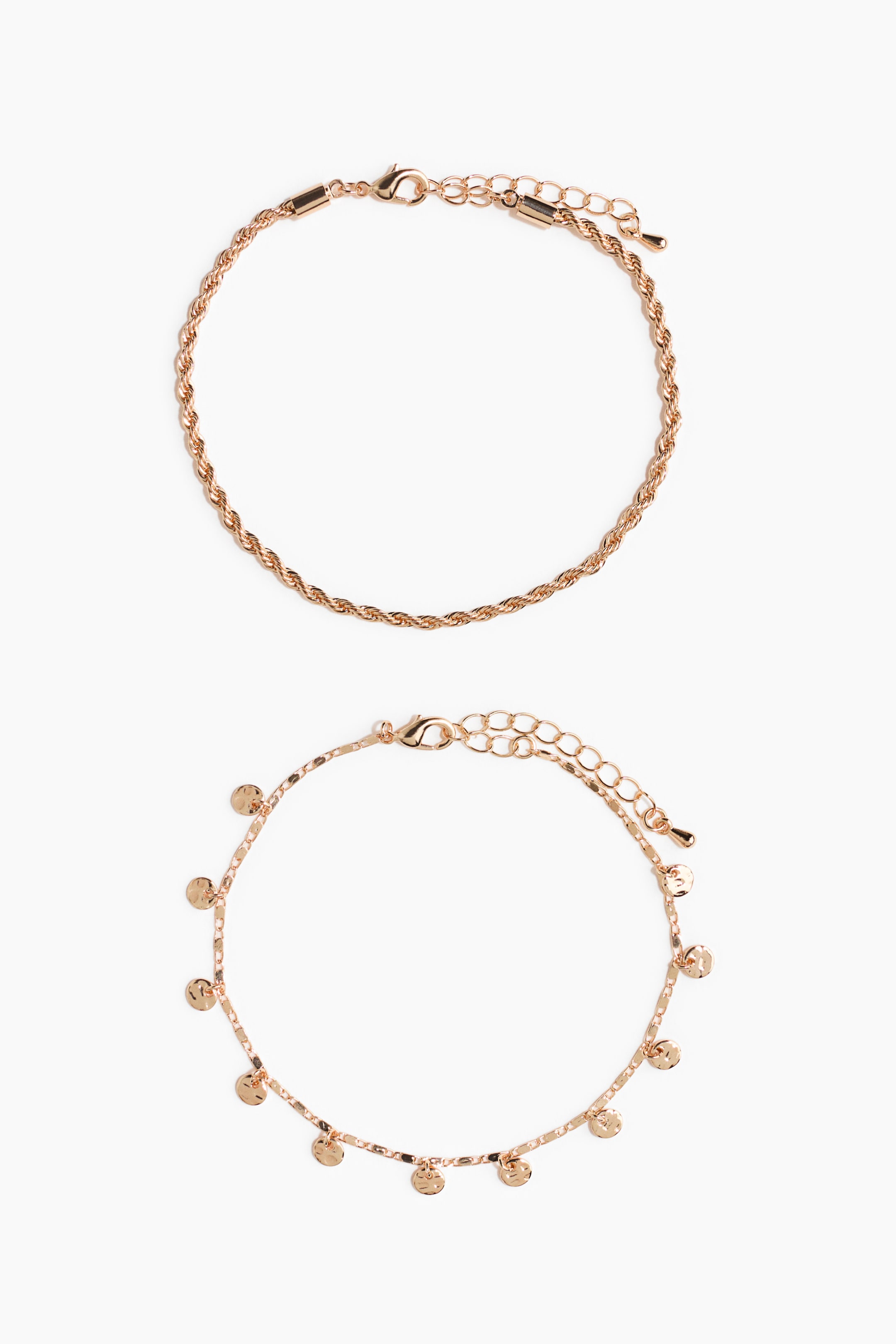 Ver imagen más grande: Dos tobilleras de oro rosa están colocadas planas, cada una con un cierre de langosta y una cadena extensora. La tobillera superior presenta un diseño de cadena de cuerda, mientras que la tobillera inferior exhibe una cadena plana adornada con múltiples pequeños dijes redondos martillados.