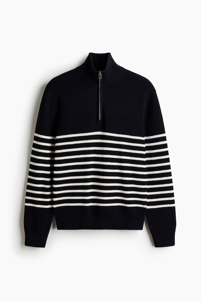 Un maglione blu navy presenta strisce orizzontali bianche lungo il corpo e le maniche. È dotato di un colletto alto a coste con chiusura a zip a un quarto di lunghezza in tonalità argento, insieme a polsini e orlo a coste. - 1