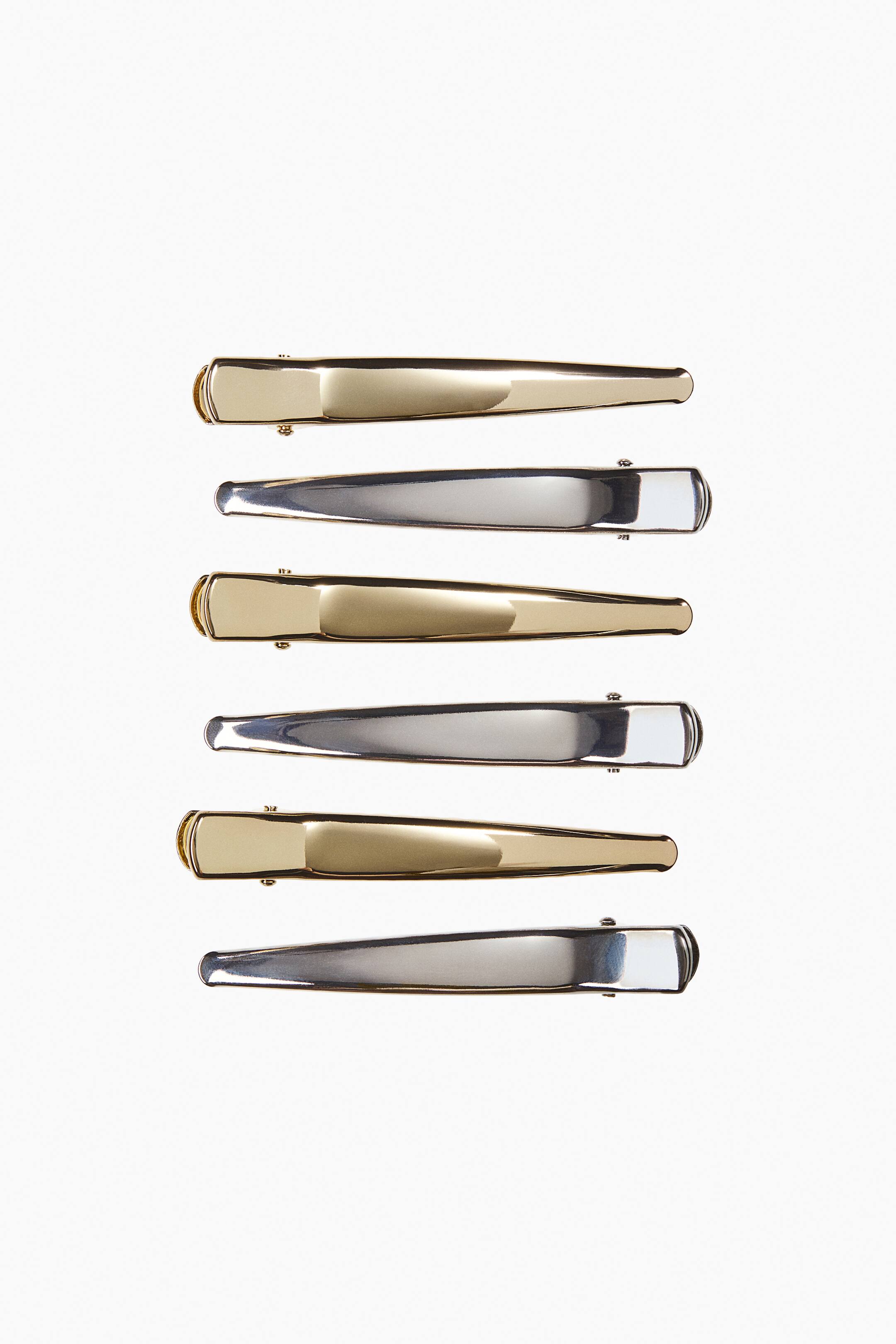 Visa större bild: Sex avsmalnande metalliska duckbill-hårklämmor ligger horisontellt i en vertikal stapel, växlande mellan polerad guld- och silverfinish.
