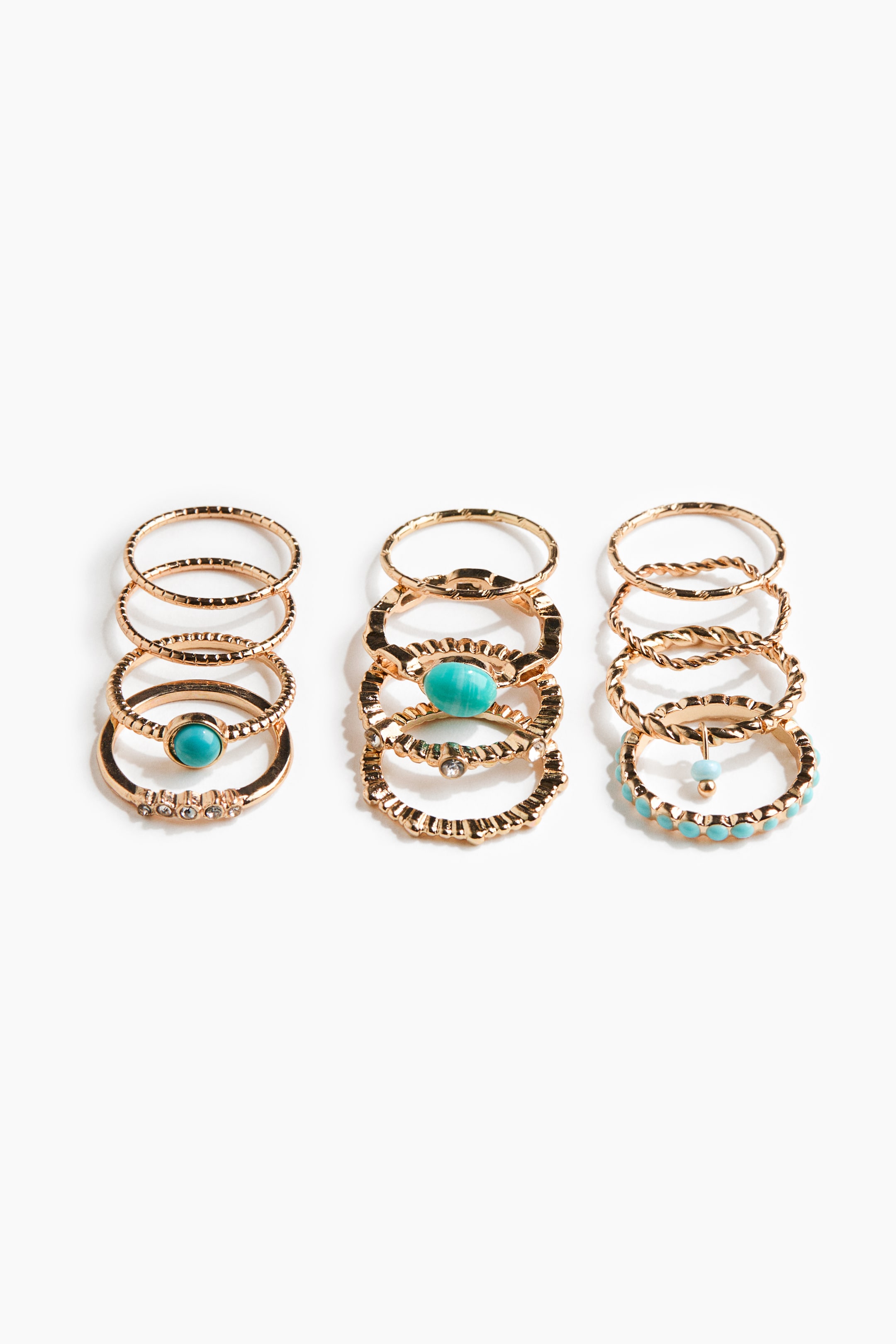 View larger image: Three vertical stacks of gold-toned rings showcase a variety of designs. The rings feature plain, textured, and twisted bands, with some bands also adorned with small clear stones, larger oval turquoise-colored stones, and small turquoise-colored beads.