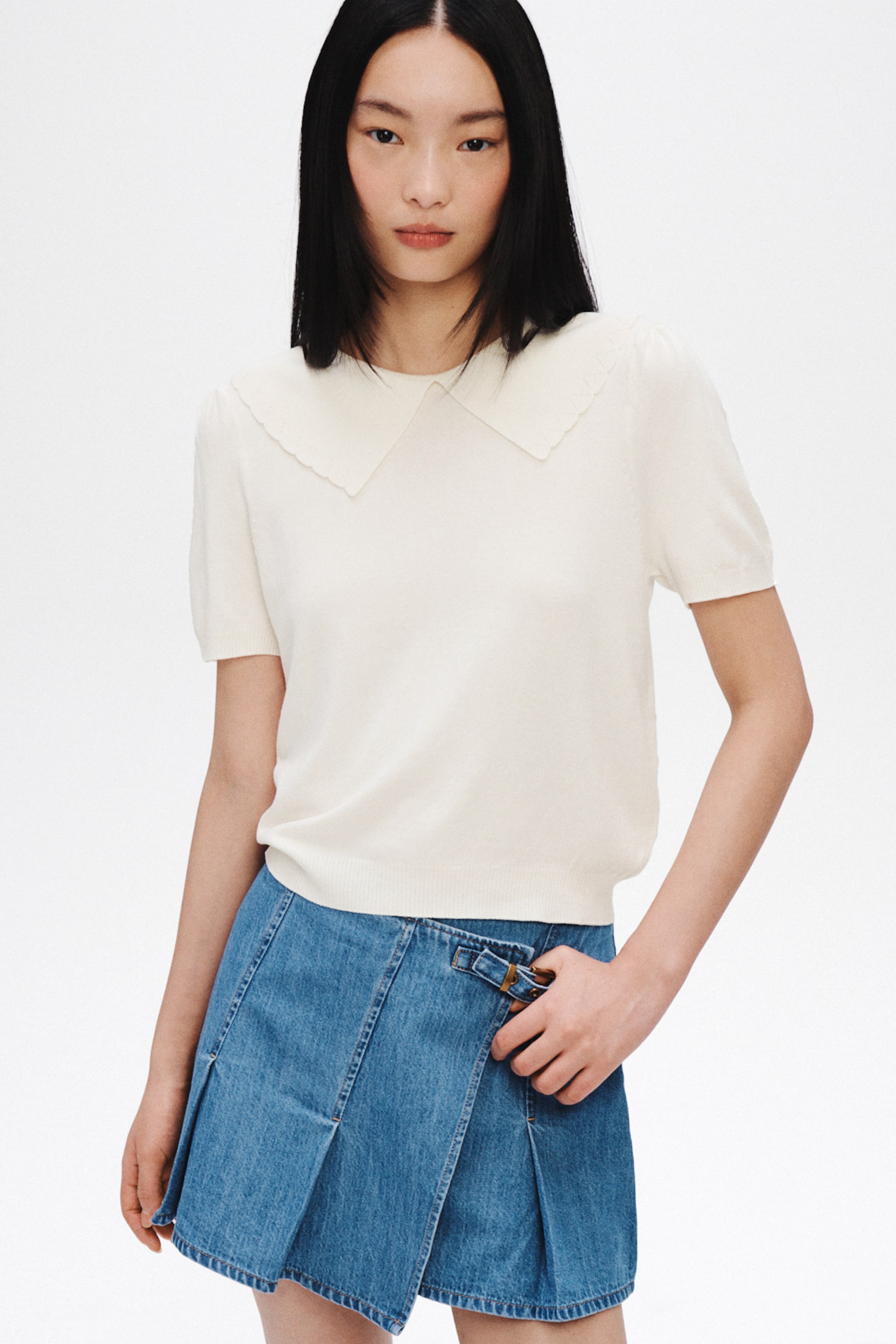 View larger image: An off-white, short-sleeved knitted top features a large scalloped Peter Pan collar. It has slightly puffed sleeves and a ribbed hem.