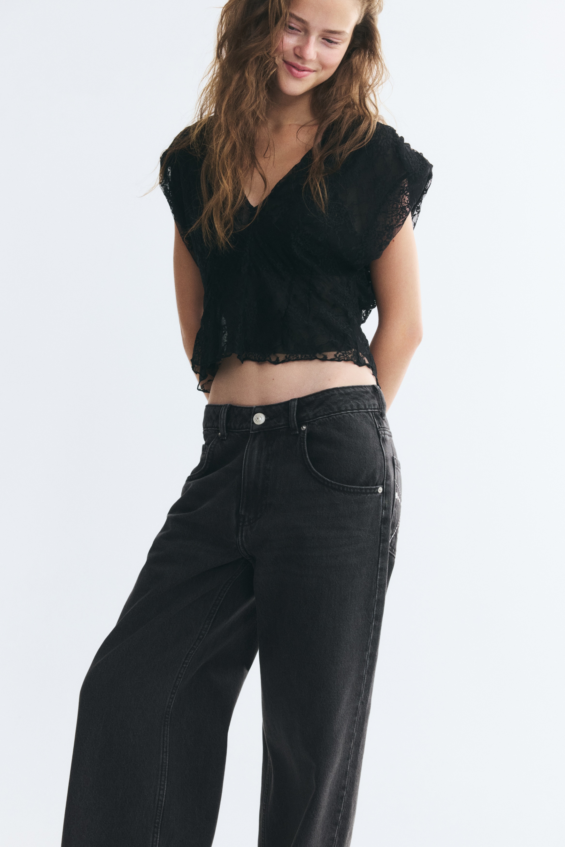 A pair of washed black denim jeans is hanging flat, facing front, showcasing a loose, straight-leg fit. The jeans feature a classic five-pocket design with a top button fastening, belt loops, and subtle fading across the upper thighs.