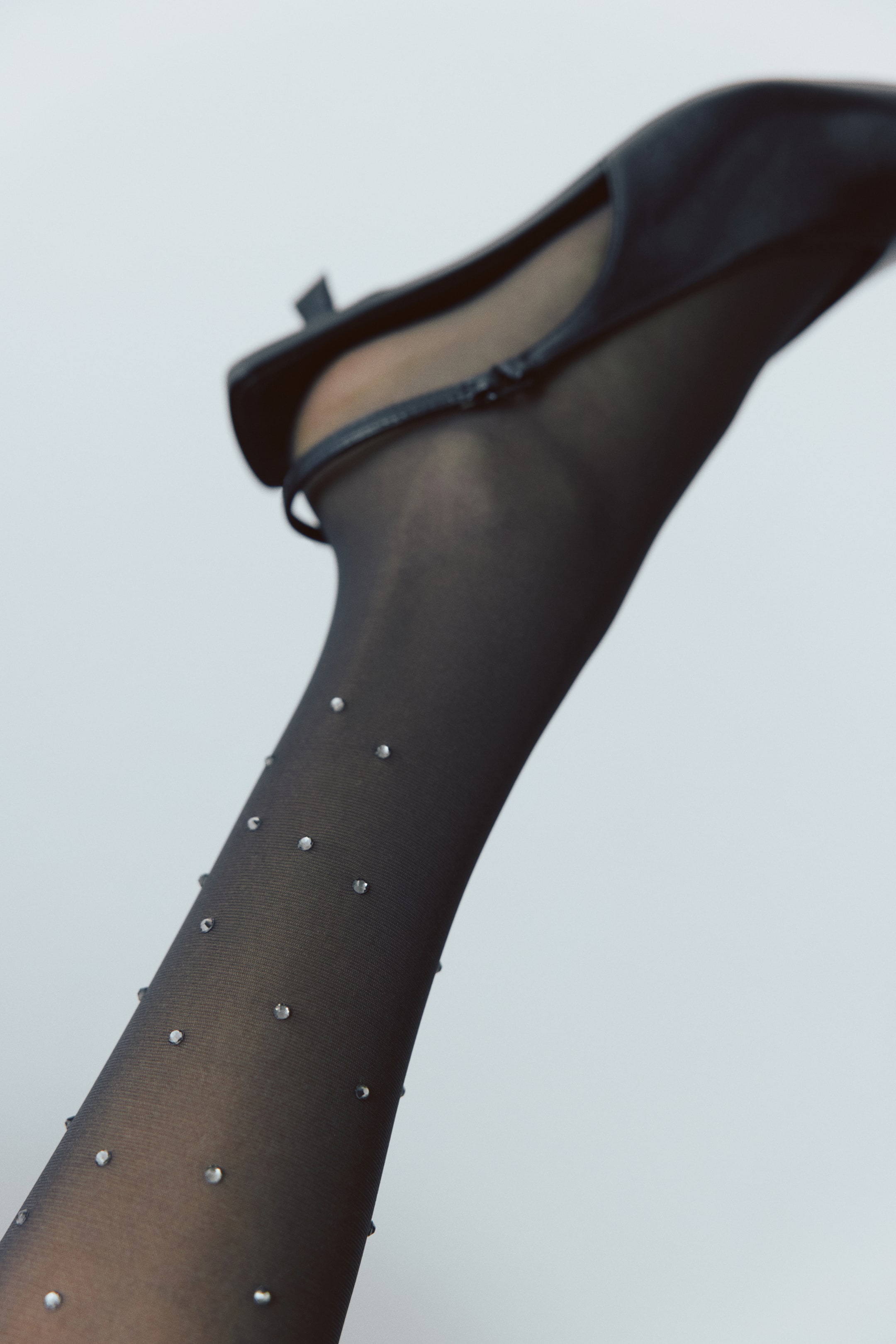 View larger image: Black semi-sheer tights embellished with small, sparkling rhinestones are being worn on a raised leg by the model. The tights are styled with a black pointed-toe slingback shoe.