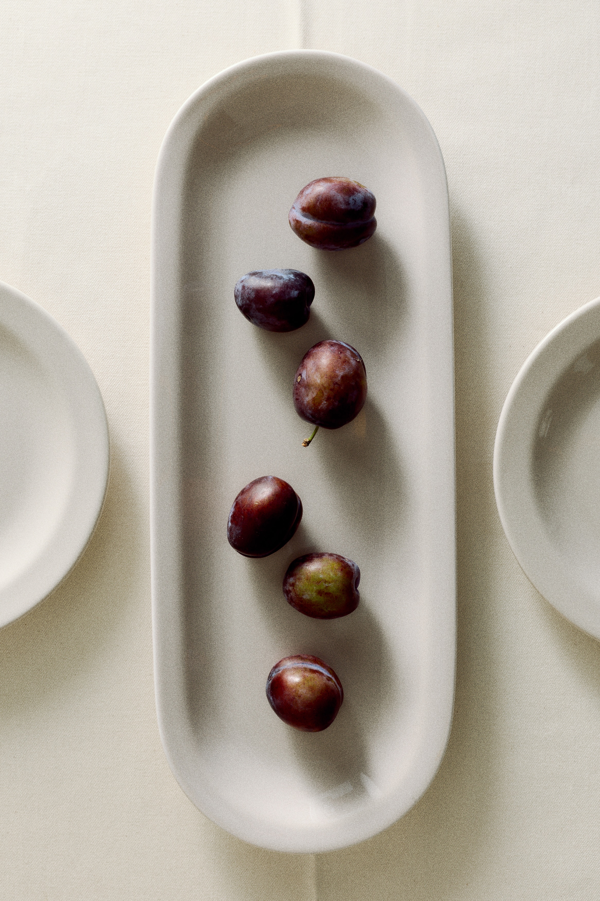 A white, glossy, elongated oval dish features a shallow well and slightly raised edges. It showcases rounded ends when viewed from directly above.