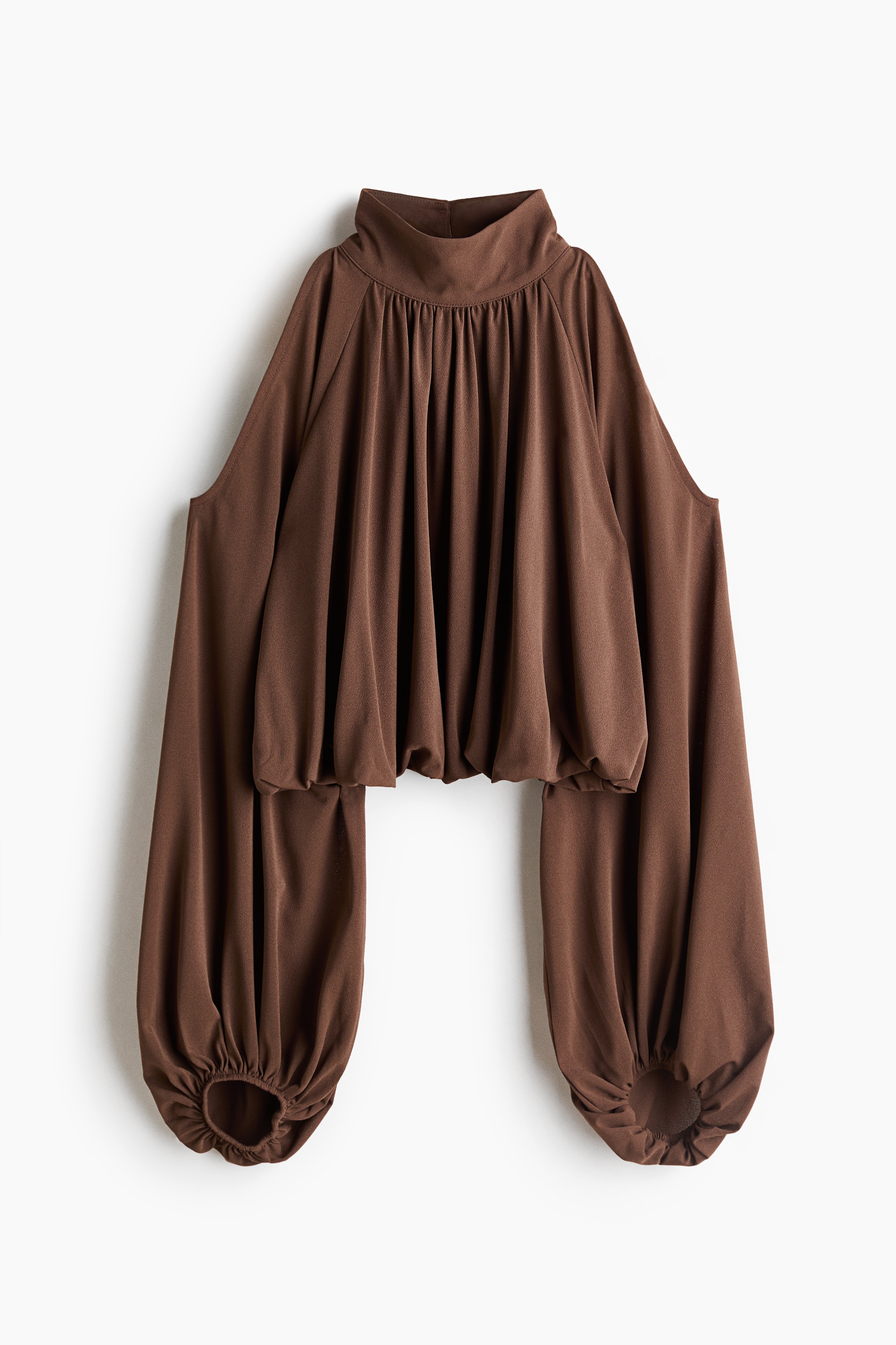 A cropped brown top in textured jersey is worn by the model, featuring a high neck, a gathered neckline for a draped effect, cold shoulders, and long balloon sleeves. The top is designed with a bubble hem and is paired with matching brown trousers.