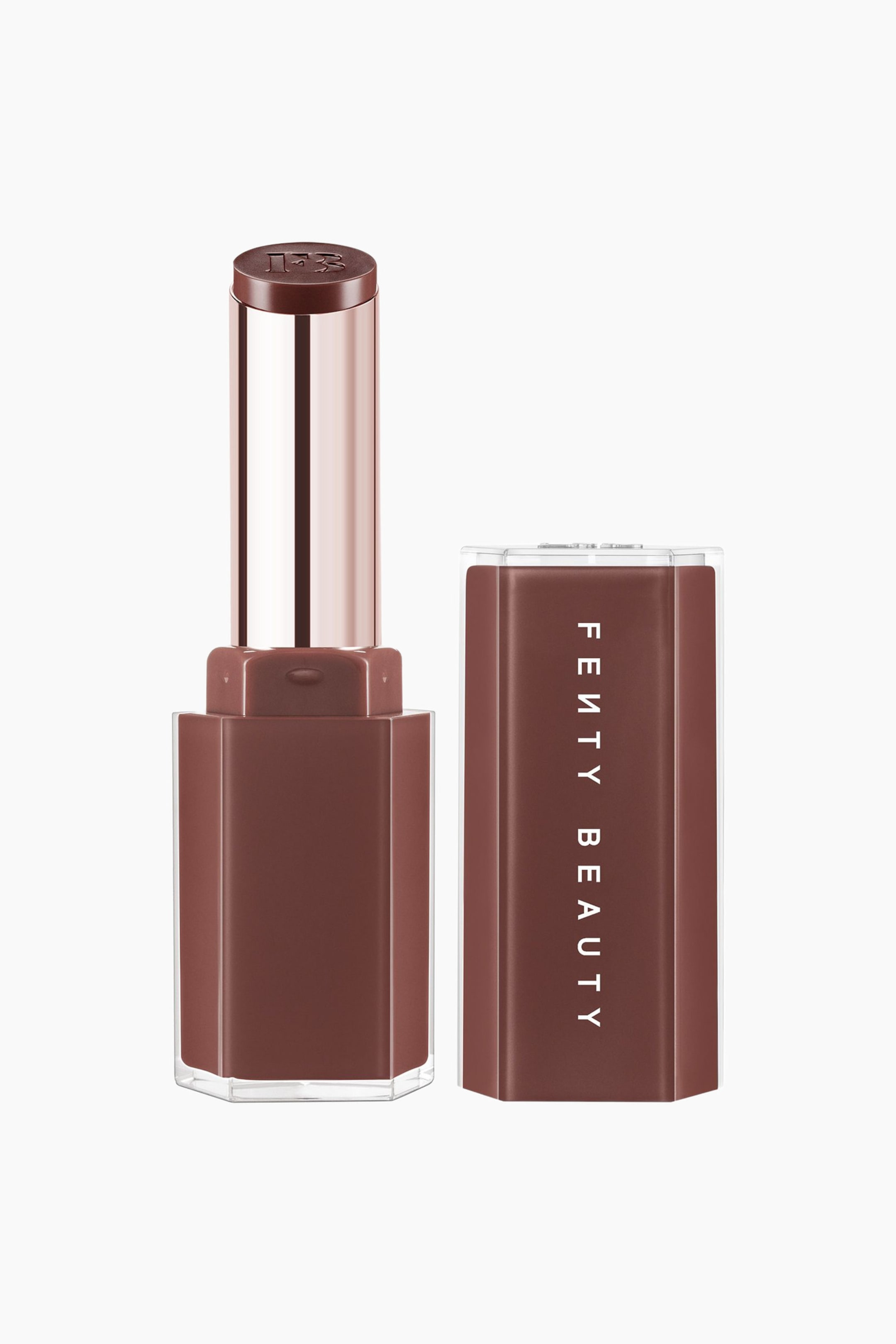 Näytä suurempi kuva: Gloss Bomb Stix High-shine Gloss Stick on pystyasennossa, ja sen metallinhohtoinen ruusukultainen sisäputki on näkyvissä. Näkyvillä on tasakärkinen, syvänruskea glossipuikko, johon on kohokuvioitu 'FB'-logo. Jalustan vieressä sen yhteensopiva kuusikulmainen ruskea korkki seisoo pystysuorassa, ja sen läpinäkyvän sivun läpi kulkeva valkoinen "FENTY BEAUTY" -brändäys on esillä.