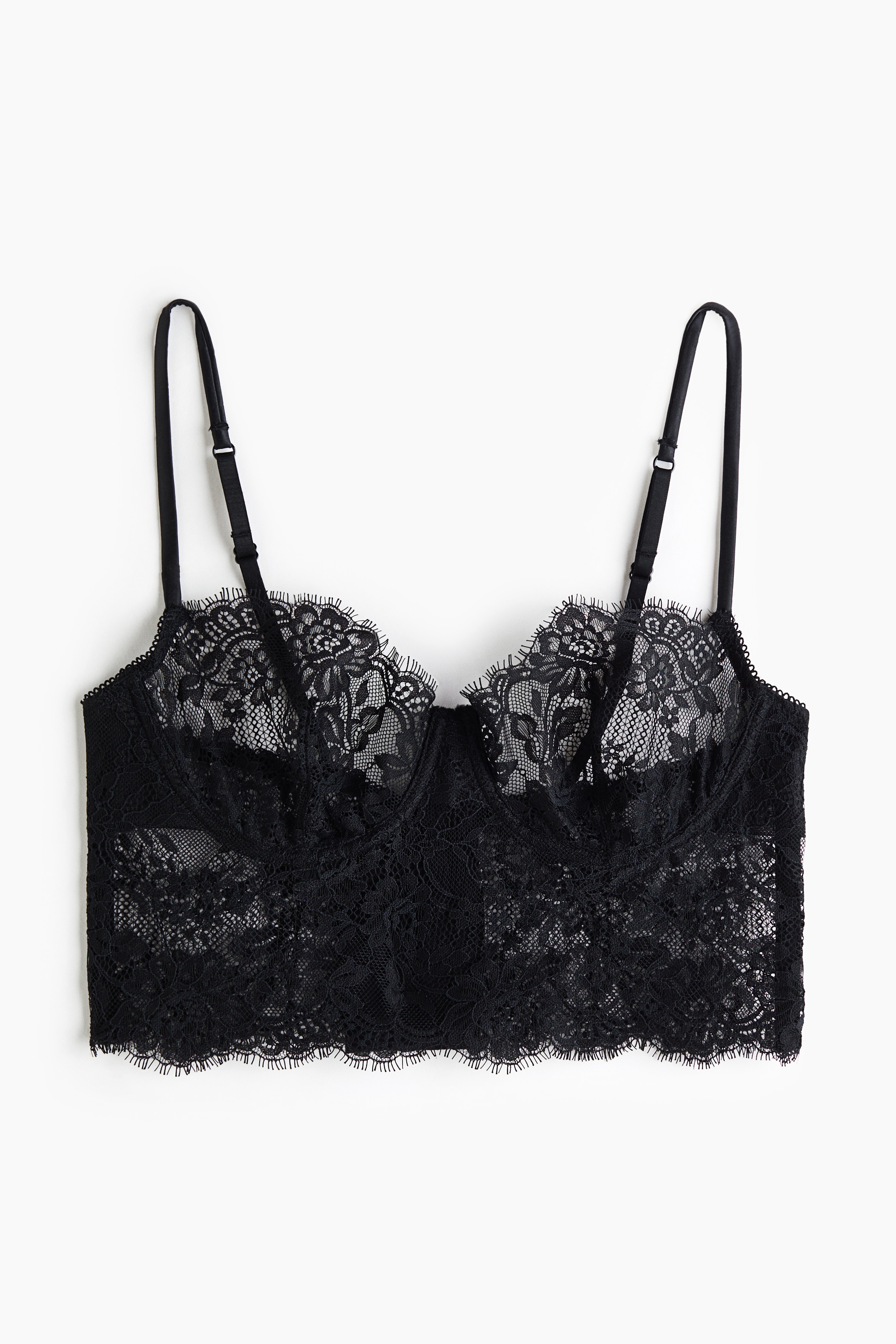 Un bralette en dentelle noire, orné d’une dentelle florale transparente, de bonnets à armatures et de fines bretelles, est porté par le mannequin. Le modèle longline est rehaussé d’une délicate bordure en dentelle à franges le long des bords festonnés des bonnets et de la bande inférieure.