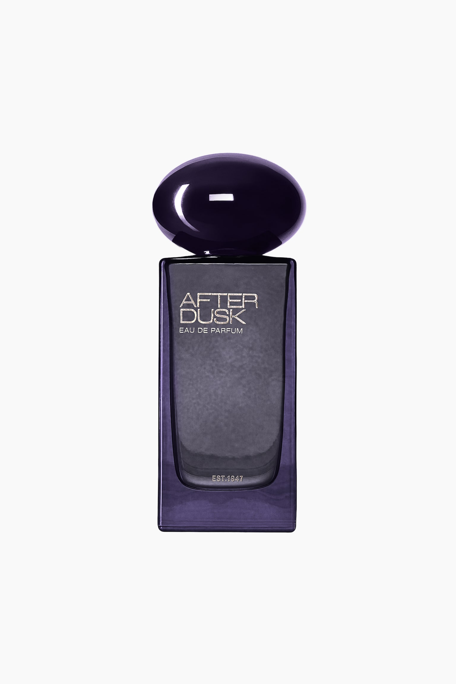 Et frontbilde av Eau de Parfum-flasken «After Dusk», med en rektangulær kropp i mørklilla glass og en strukturert frontpanel i dypgrått. Flasken er toppet med en blank, avrundet kork i dyp lilla, formet som en liten stein, og har sølvfarget tekst med «AFTER DUSK EAU DE PARFUM» og «EST.1947».