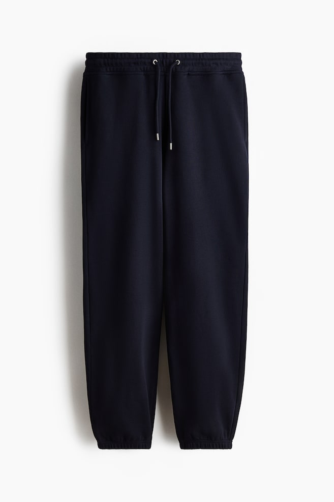Navy sweatpants crafted from cotton sweatshirt fabric showcase a laid-back fit from the front, boasting a covered elastic waistband with a visible drawstring, subtle side seam pockets, and elasticated cuffs. - 1