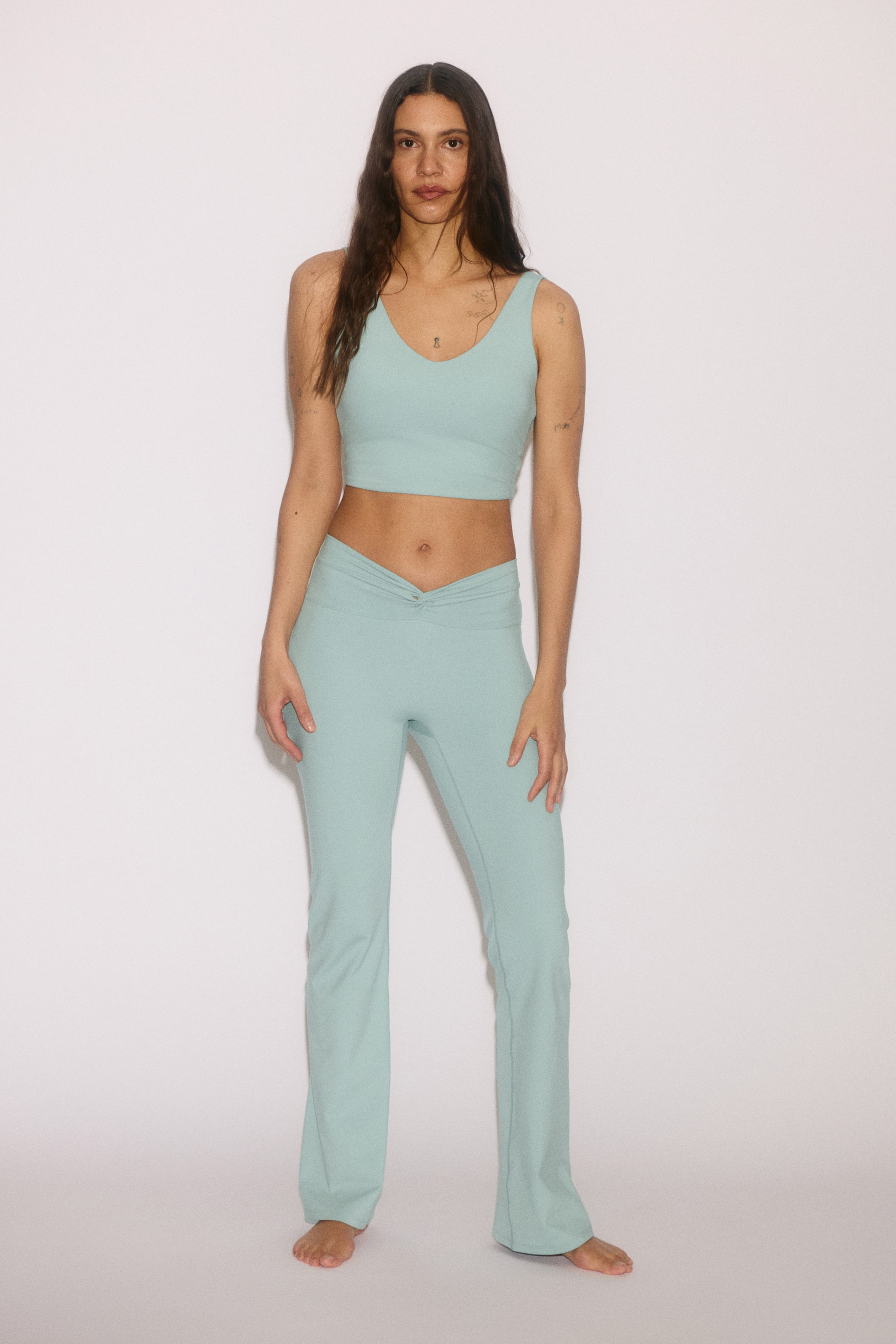 View larger image: The model is wearing a light blue cropped vest top with a v-neck. She pairs it with matching light blue pants that have a twisted waistband detail.