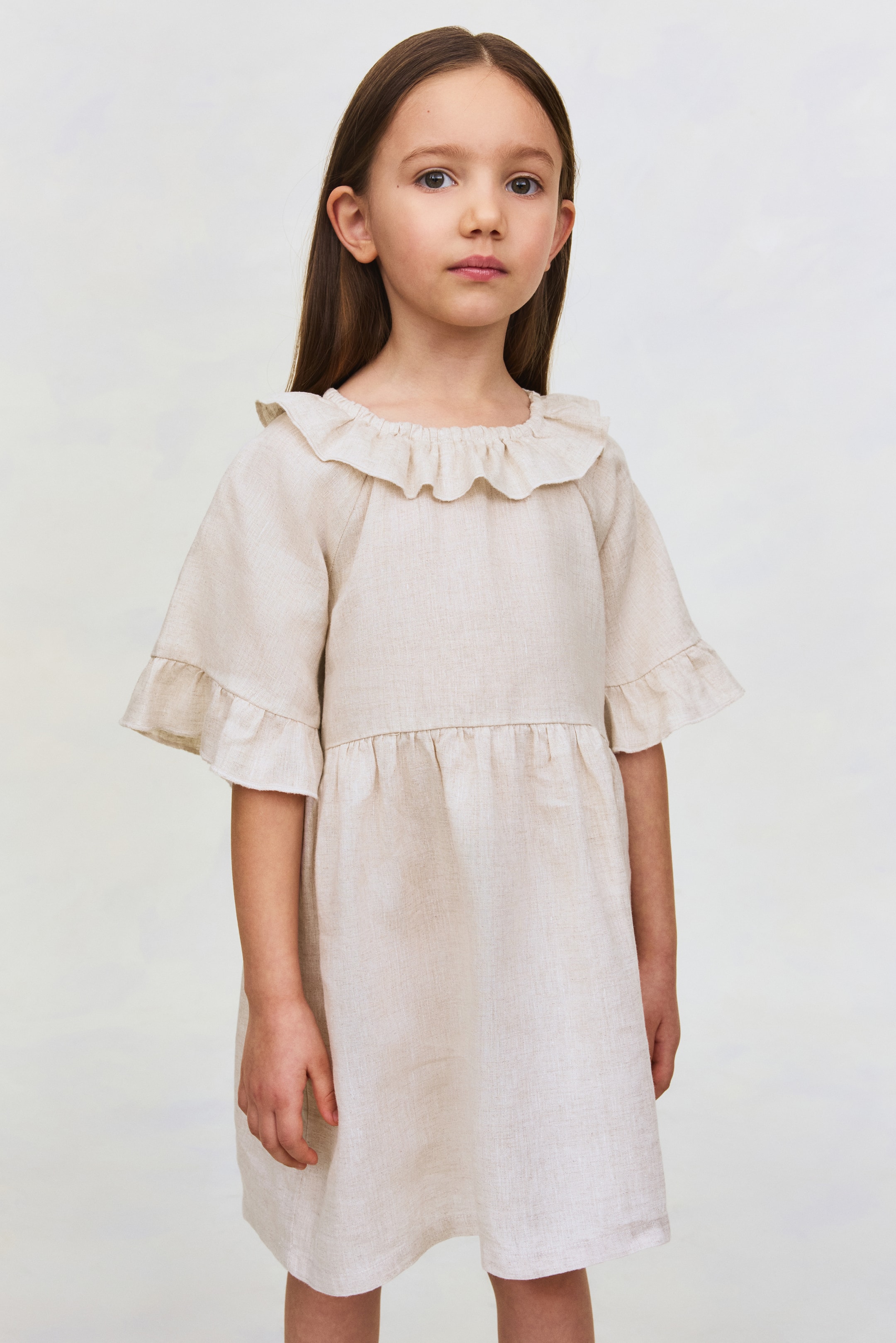 View larger image: This light beige linen dress features a ruffled round neckline. It has short, wide sleeves with ruffled cuffs and a gathered seam at the waist that leads to an A-line skirt.