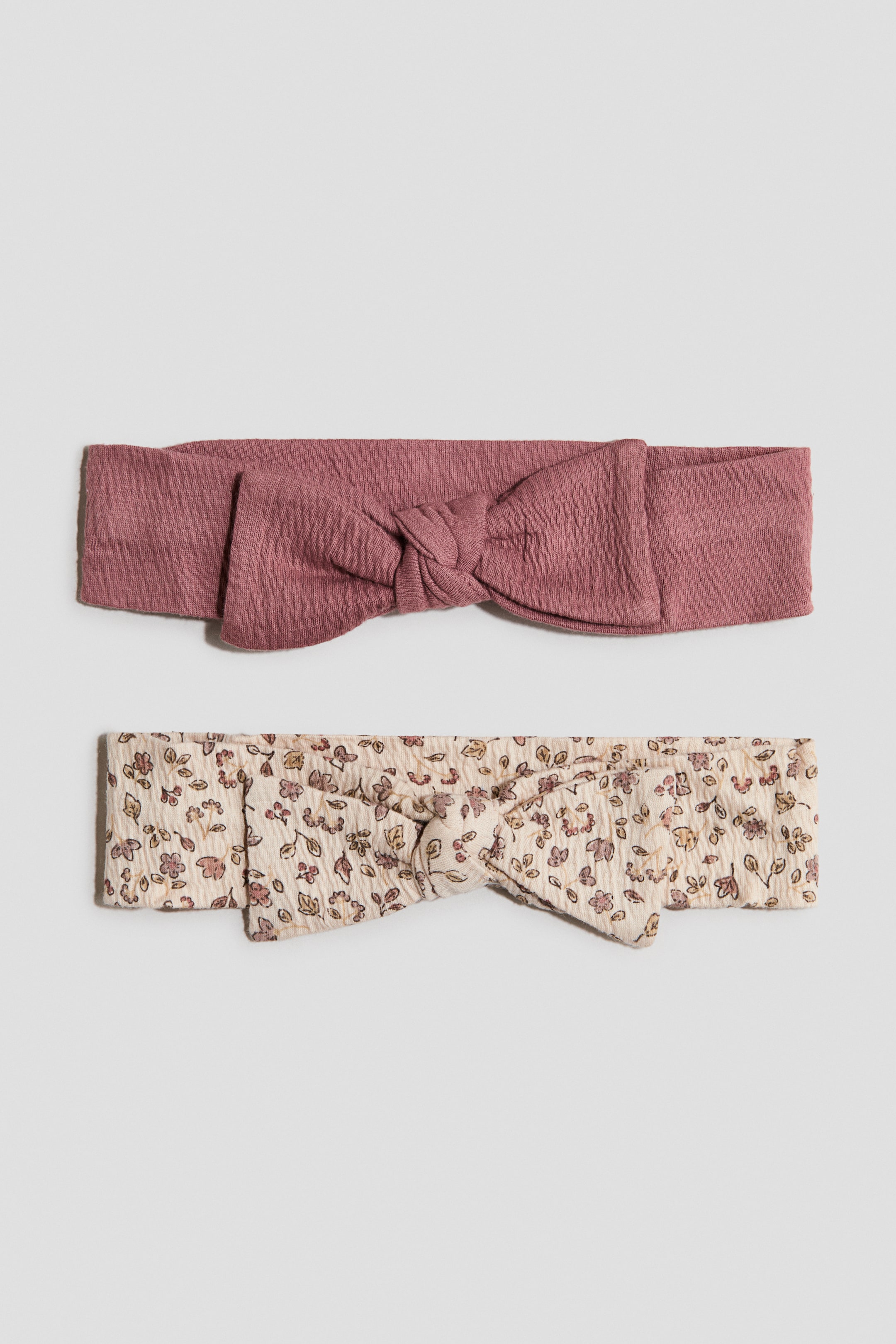 Agrandir l'image: Deux bandeaux texturés sont disposés horizontalement, chacun doté d'un nœud central. Le bandeau du haut est rose poussiéreux, tandis que celui du bas est crème avec un petit imprimé floral.