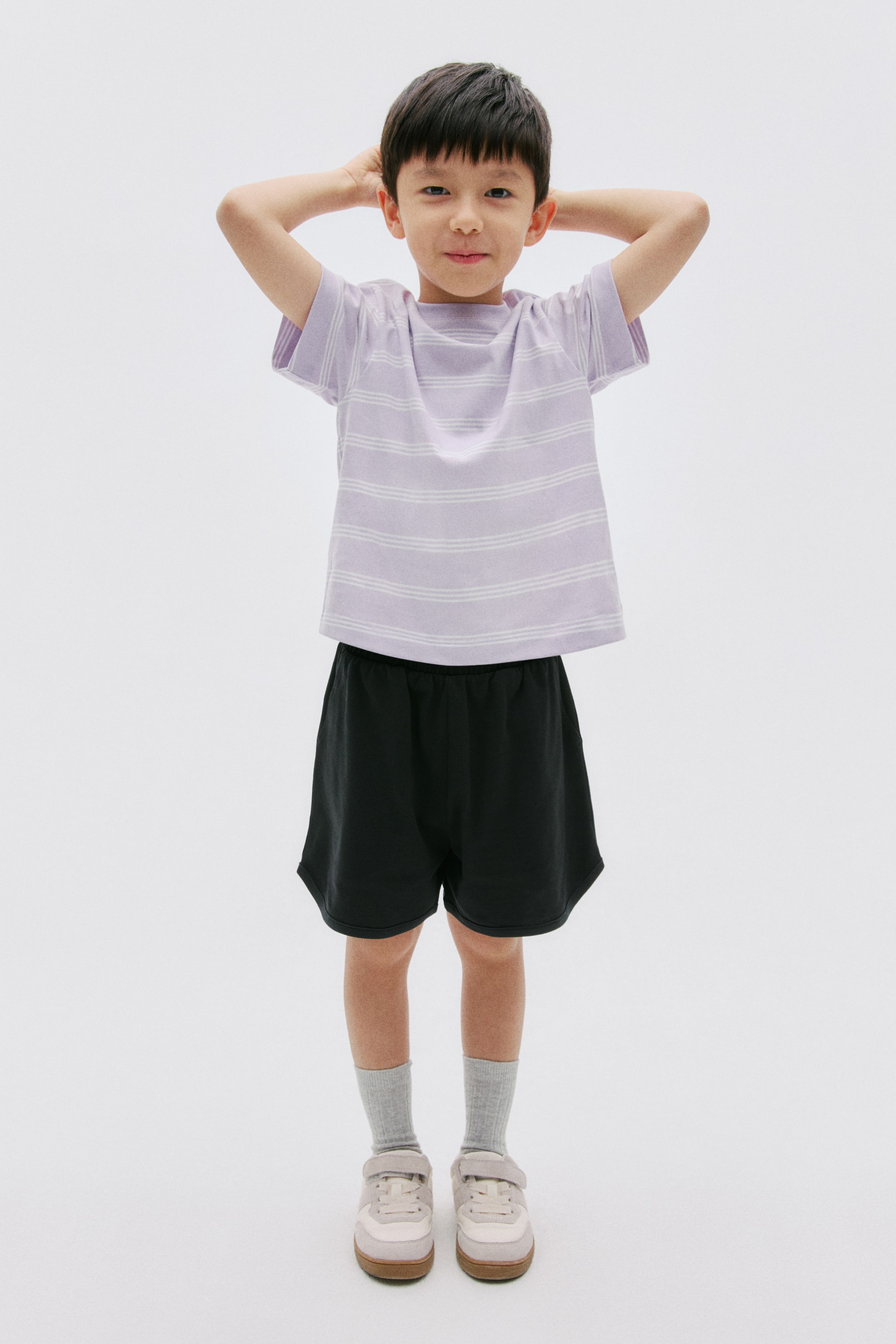 View larger image: A lavender t-shirt with white horizontal stripes and black shorts are being worn by the model. The t-shirt features a crew neck and short sleeves, while the shorts have an elastic waistband.