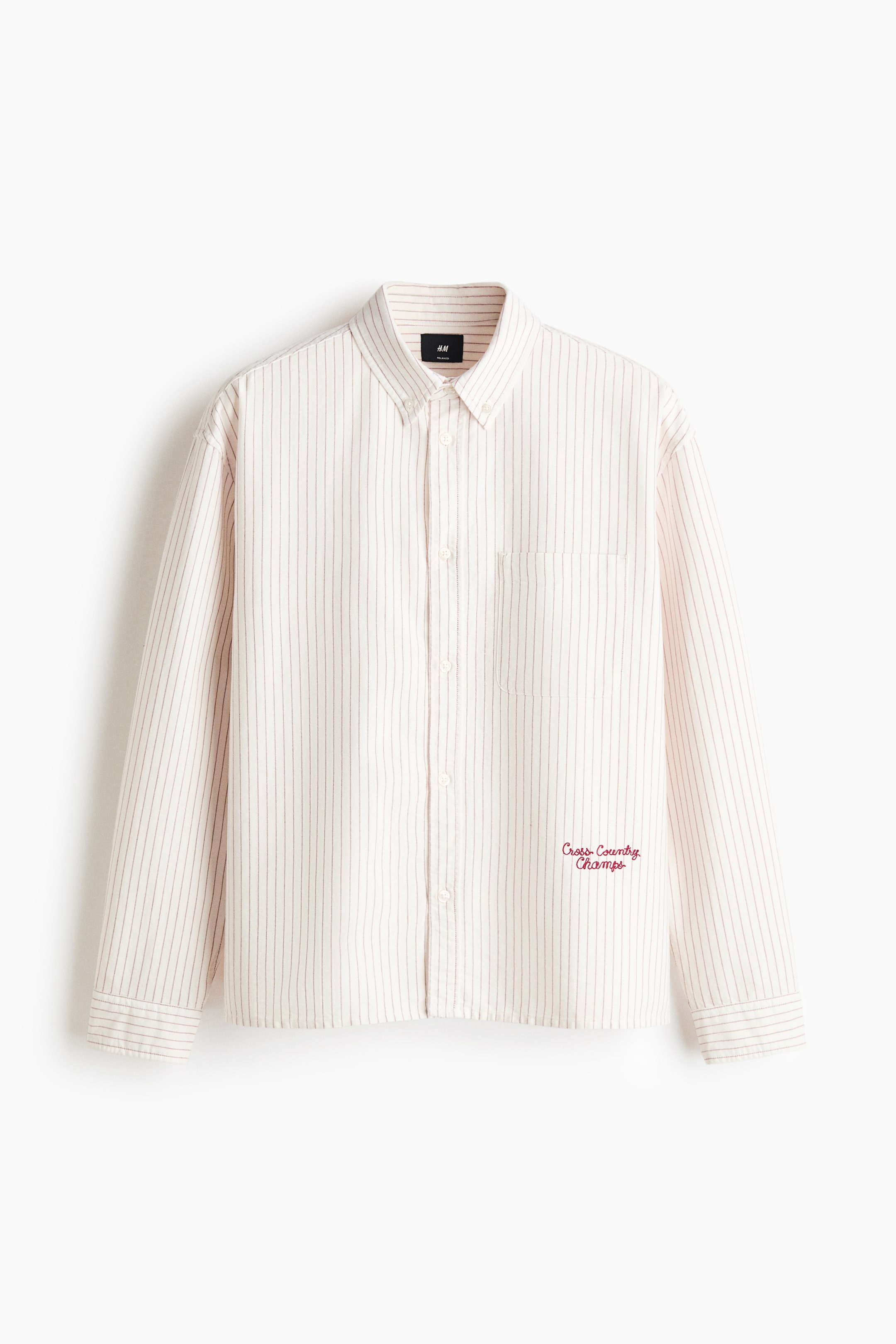View larger image: A front-facing view of a relaxed-fit Oxford cotton shirt is showcasing vertical red pinstripes on a light cream background, a button-down collar, and a button-up front. The shirt is displaying long sleeves, an open chest pocket, and a red embroidered script motif reading "Cross Country Champs" on the lower left.