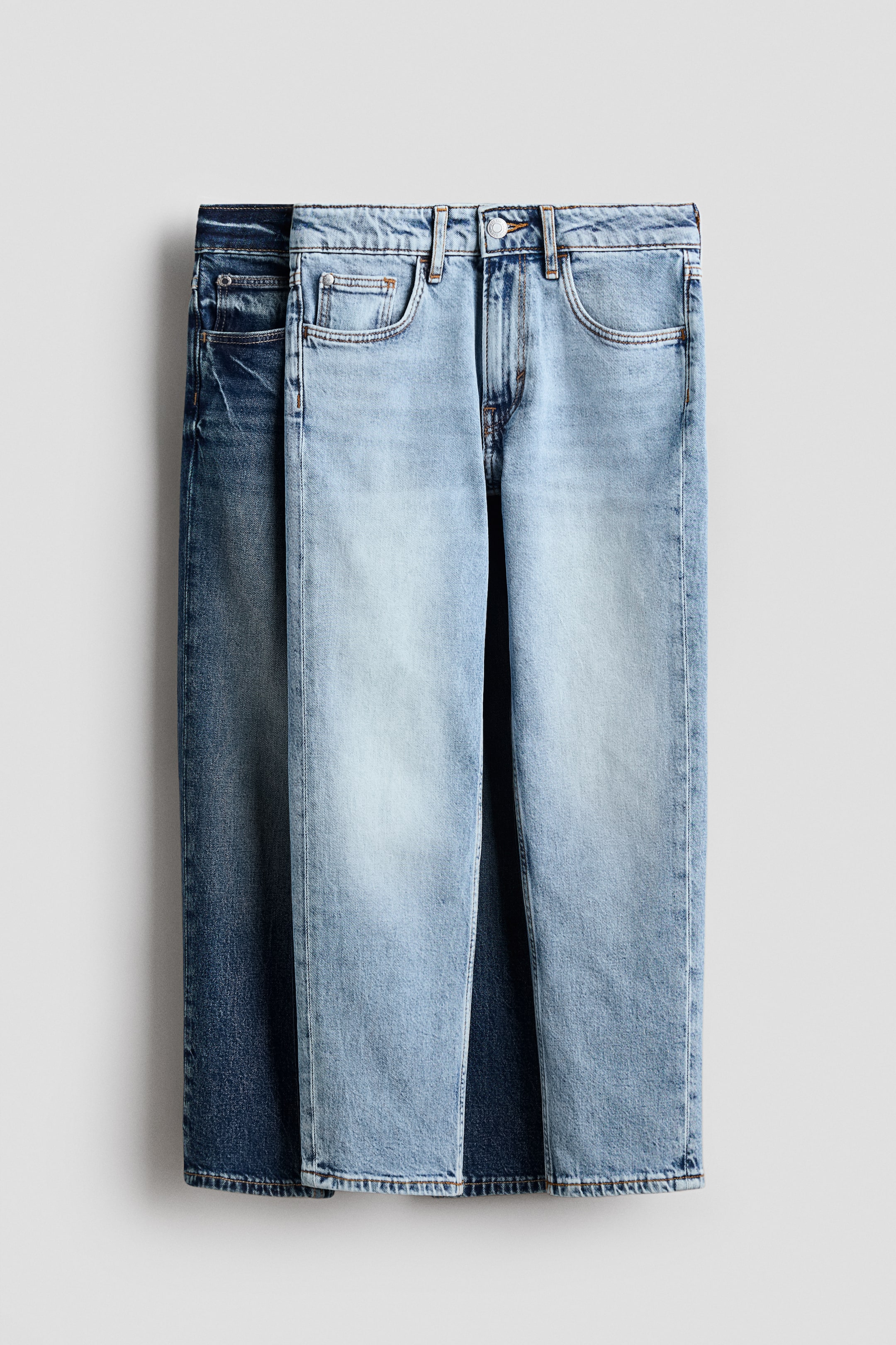 View larger image: Two pairs of 5-pocket jeans are presented front-on, with a light-wash blue denim pair in front and a darker-wash blue denim pair partially visible behind it. The front pair features a waistband with belt loops, a button closure, a zip fly and front pockets, including a coin pocket, displaying a relaxed fit with tapered legs.