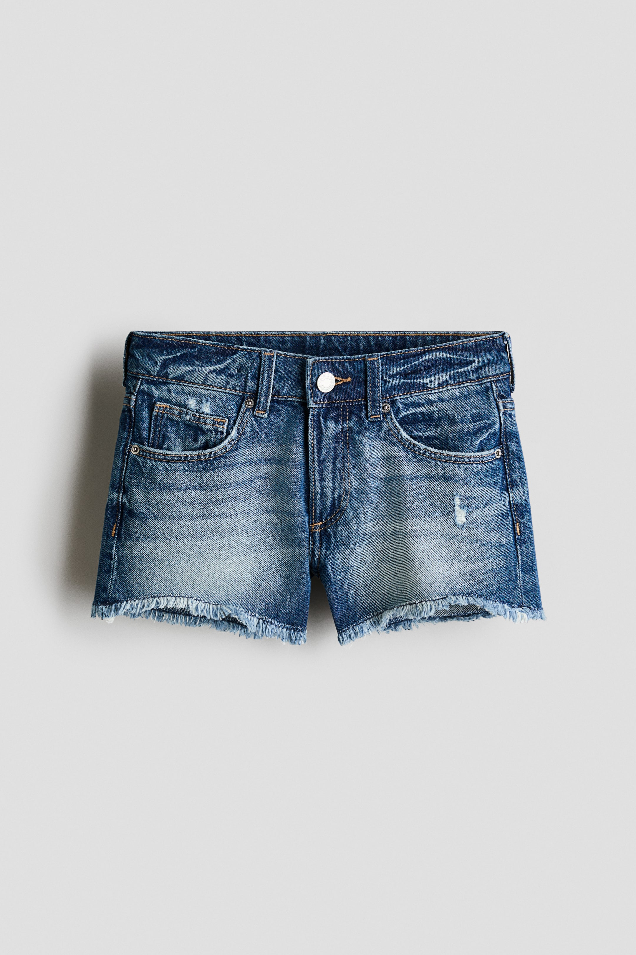 View larger image: Denim shorts are shown from the front, featuring a medium-blue faded wash with whiskering and a distressed patch on the right thigh. They have a front button closure, belt loops, two front pockets, a coin pocket and a frayed raw hem.
