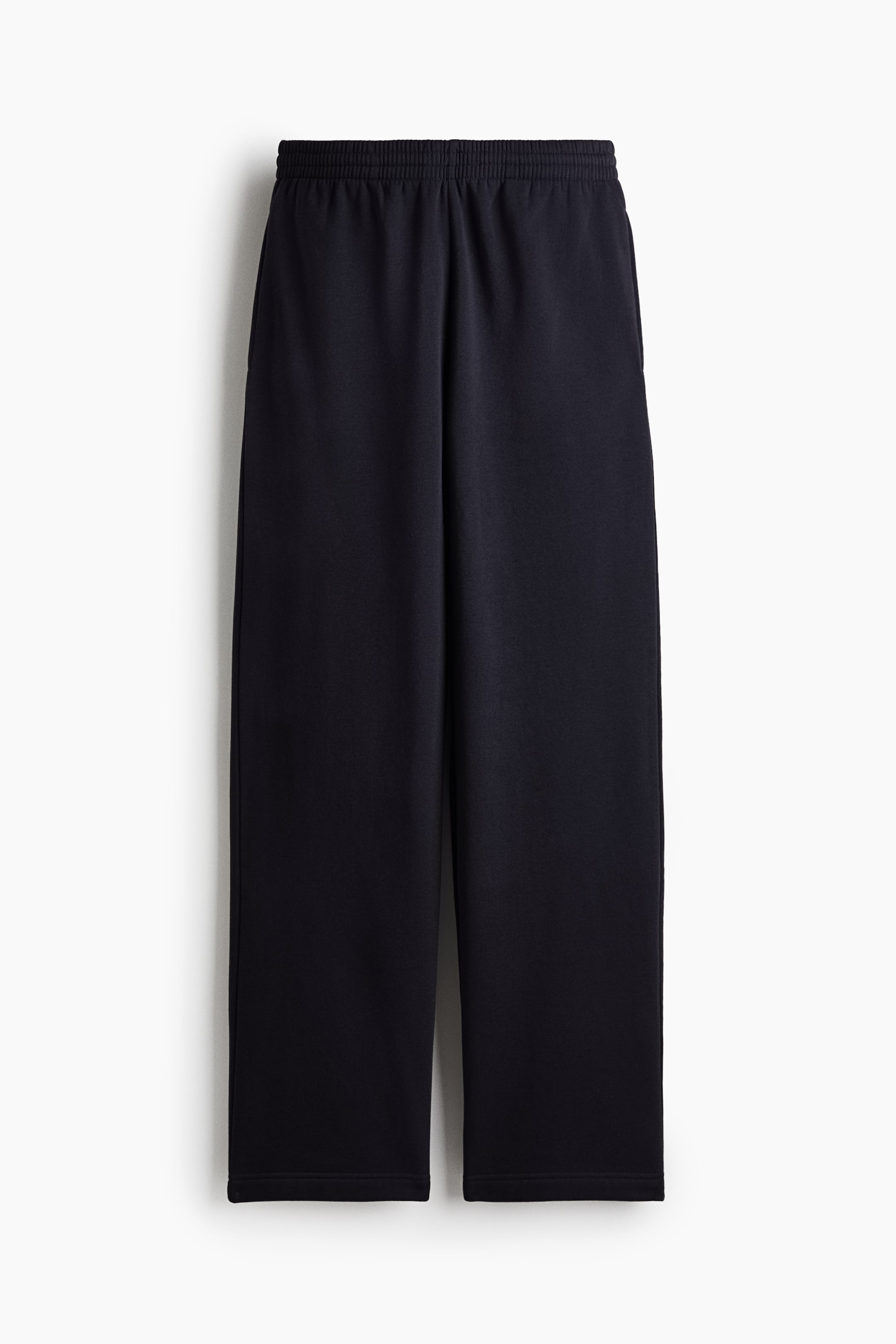 View larger image: A pair of black track pants is shown from the front, featuring an elasticised smocked waistband and straight legs. The pants fall straight, showcasing their relaxed fit and smooth sweat fabric texture.