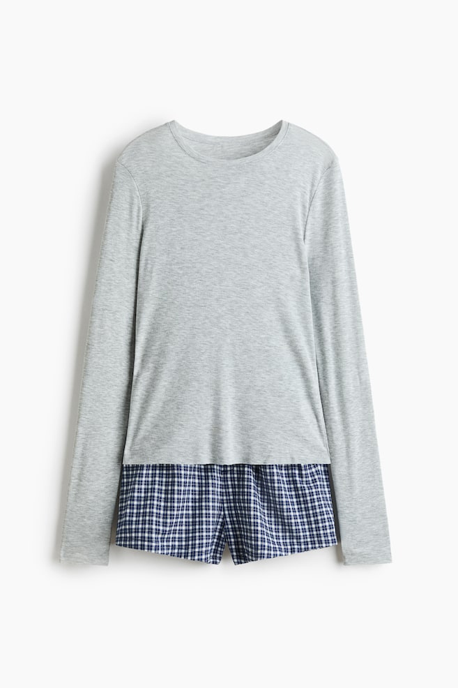 A two-piece pajama set is displayed from the front, featuring a light gray, long-sleeved knit top with a crew neck layered over a pair of blue and white plaid shorts that are visible at the hem. - 1