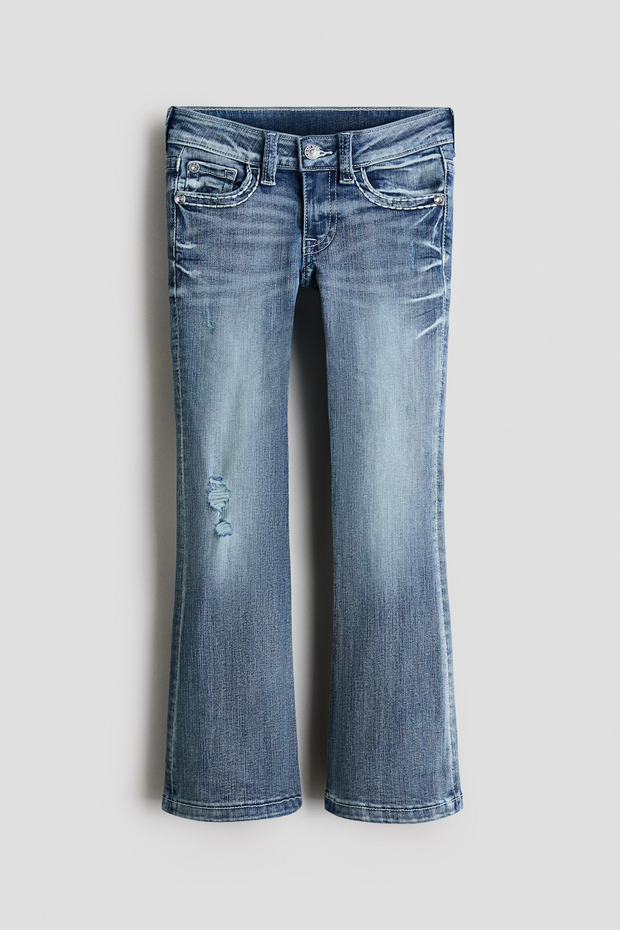 Größeres Bild anzeigen: Jeans aus gewaschenem Denim präsentieren sich in einer Vorderansicht, mit niedriger Taille, Reißverschluss und Knopfverschluss, sowie Vordertaschen und einer Münztasche. Sie zeigen abgenutzte Details, einschließlich Whiskering an den Oberschenkeln und einem abgenutzten Patch am linken Bein, und sind mit einer engen Passform von der Taille bis zum Oberschenkel gestaltet, die sich ab dem Knie bis zum Saum zu einem Bootcut-Bein ausweitet.