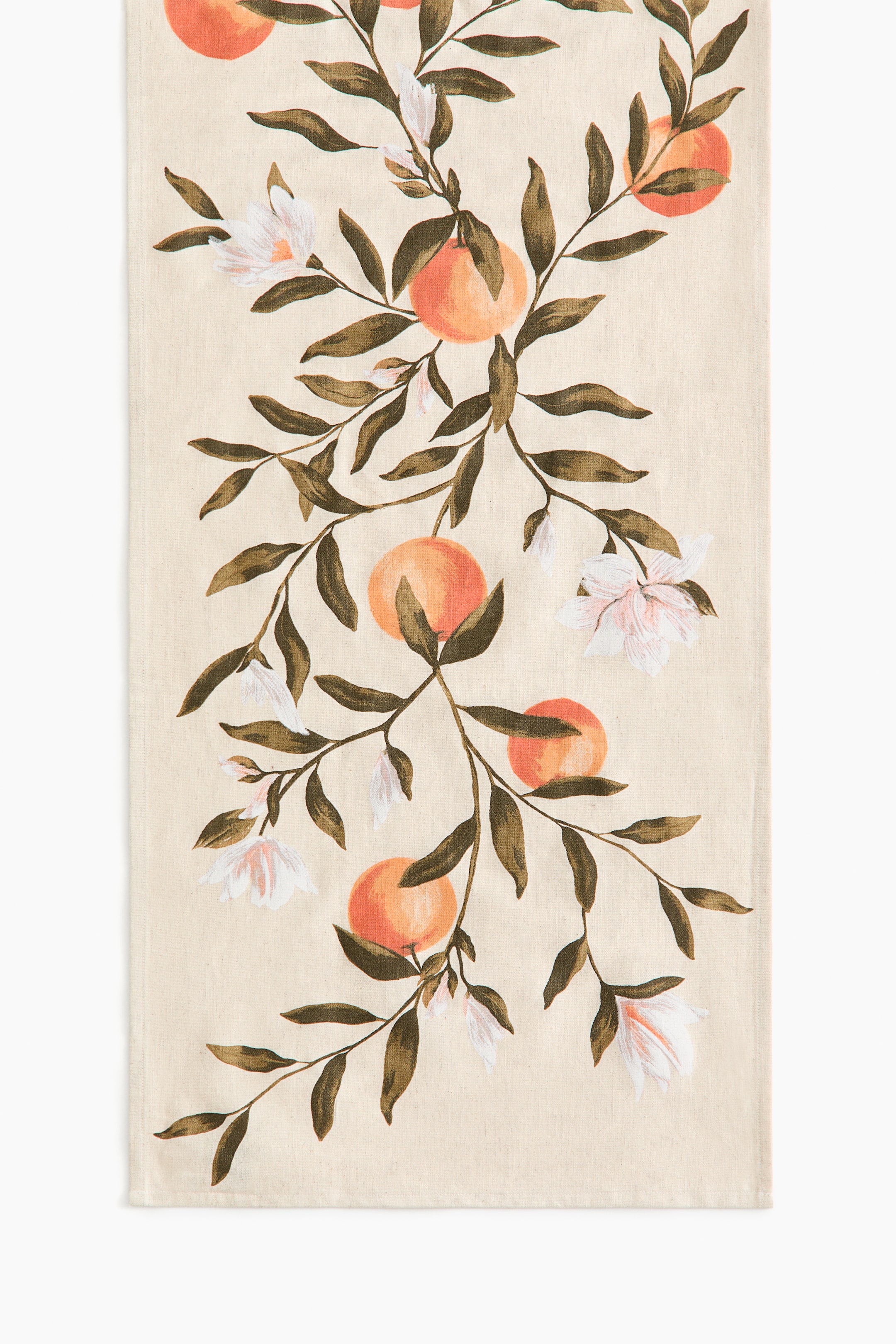 View larger image: A cream fabric runner is printed with a repeating botanical pattern featuring branches, muted green leaves, orange-colored citrus fruits, and white blossoms with subtle pink centers, flowing vertically along its length.