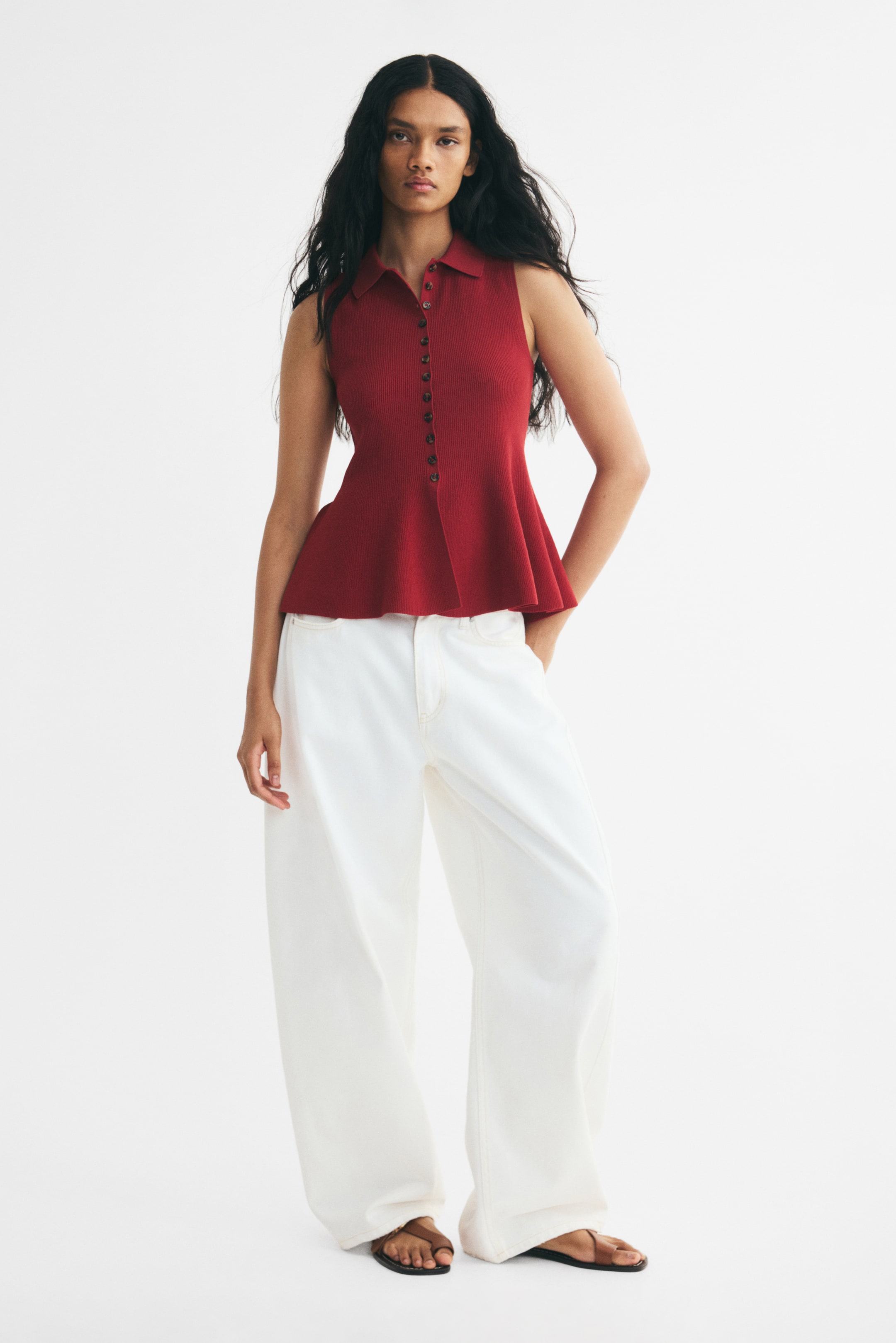 View larger image: A dark red, sleeveless rib-knit top featuring a collar, front buttons down to the waist, and a flared peplum hem is being worn by the model. The slim-fit top is styled with wide-leg white trousers.